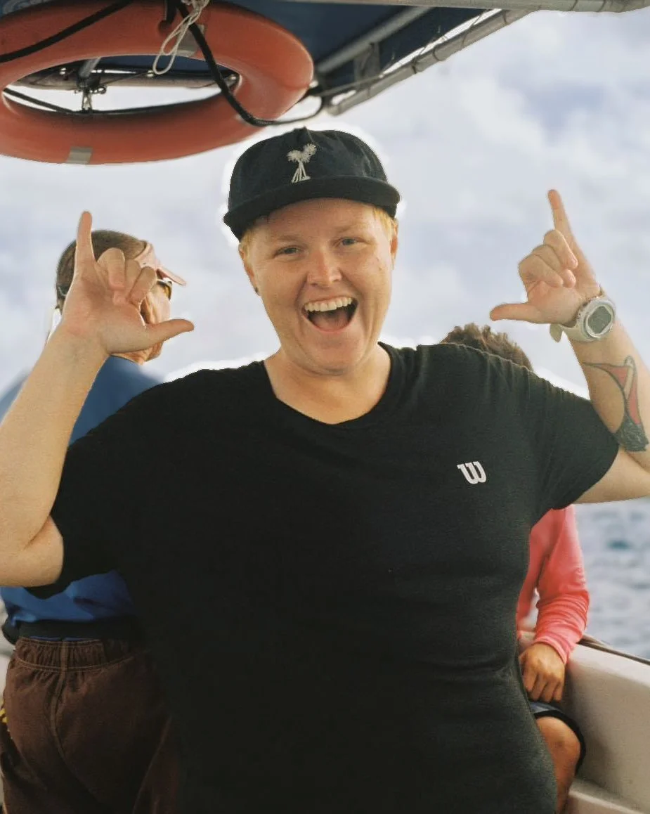 A young man with red hair smiling and making a shaka sign with both hands on a boat, with water and sky in the background.  Cozumel Scuba Diving Dive with k8