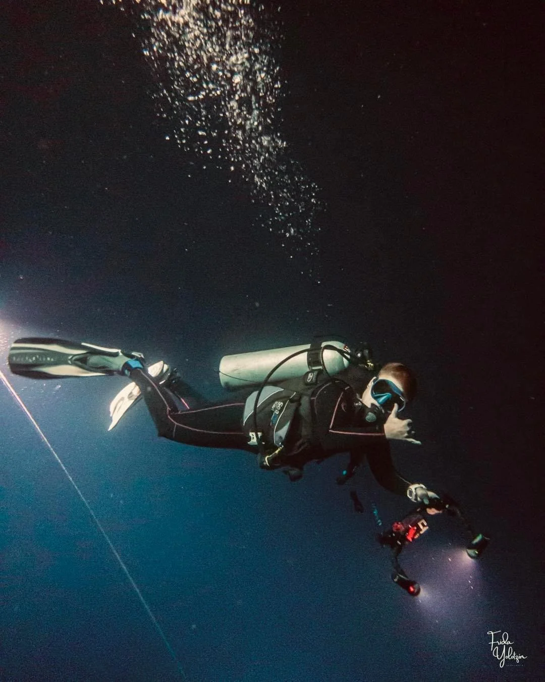 Scuba diver underwater at night with a flashlight, giving a thumbs-up, surrounded by dark ocean water and bubbles.  Cozumel Scuba Diving Dive with k8