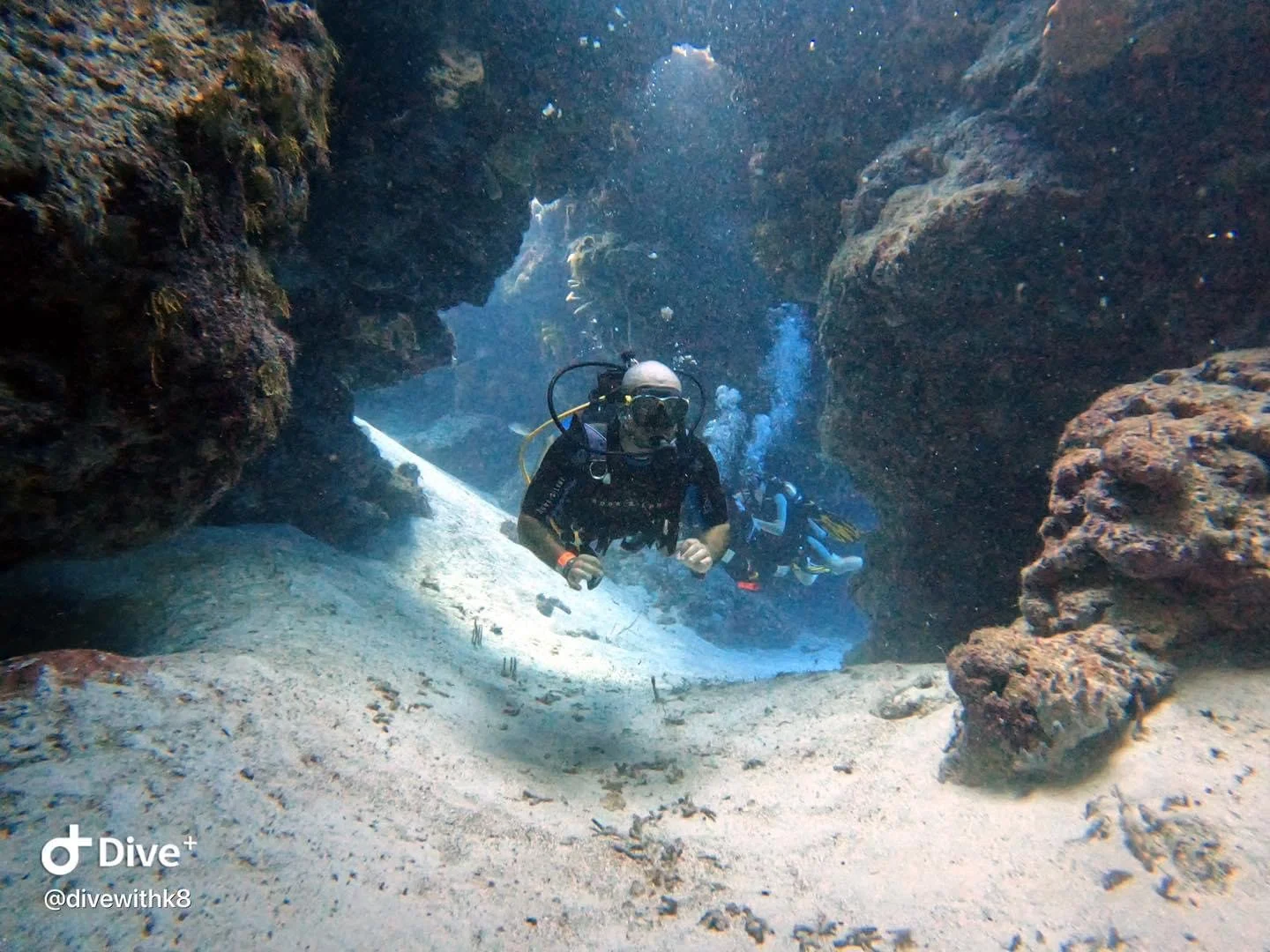 A scuba diver swimming through a narrow underwater canyon with rocky walls and sandy floor.  Cozumel Scuba Diving Dive with k8