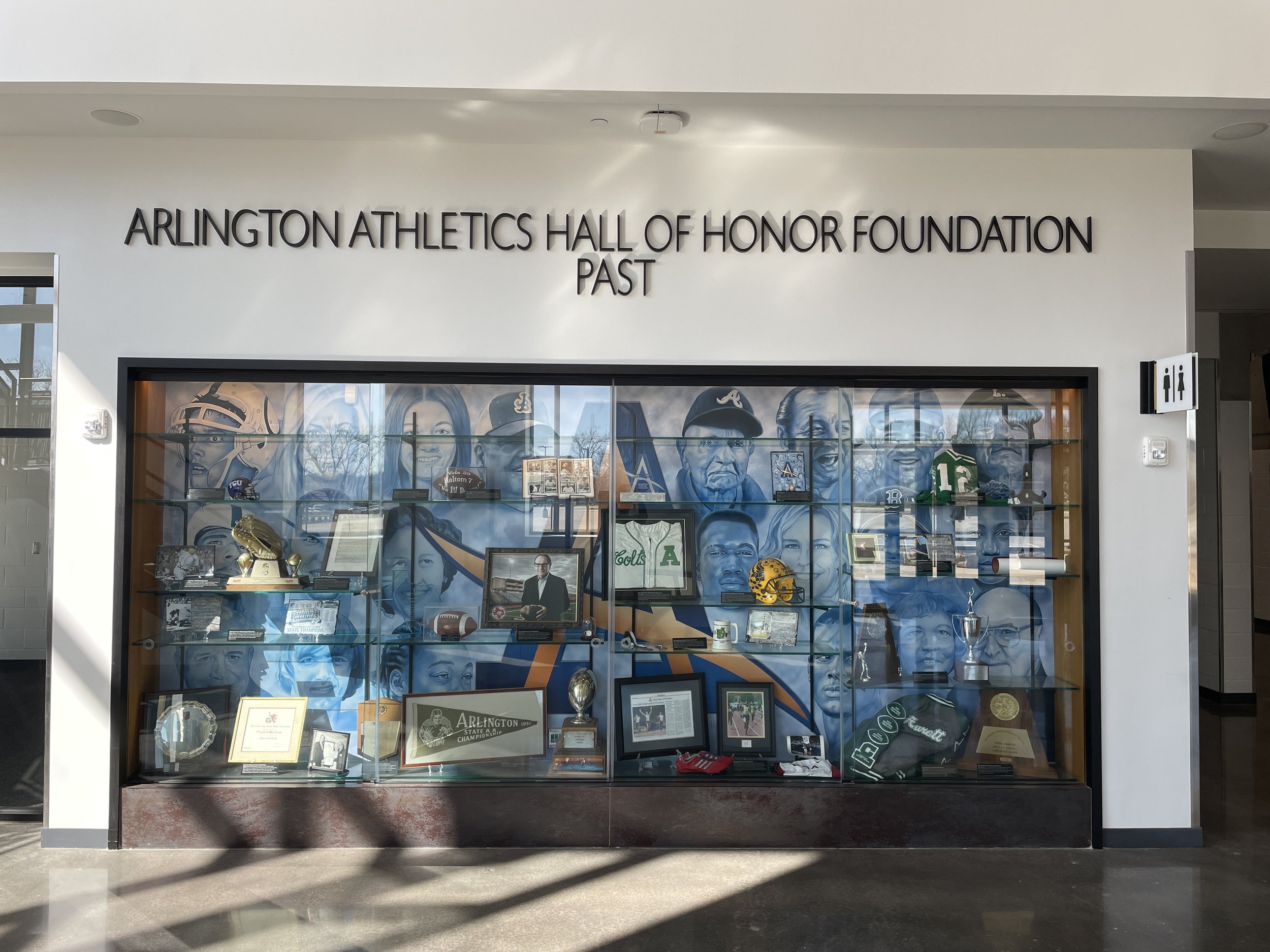 Display case at Arlington Athletics Hall of Honor Foundation featuring sports memorabilia, photos, and portraits of notable athletes and figures associated with Arlington sports.