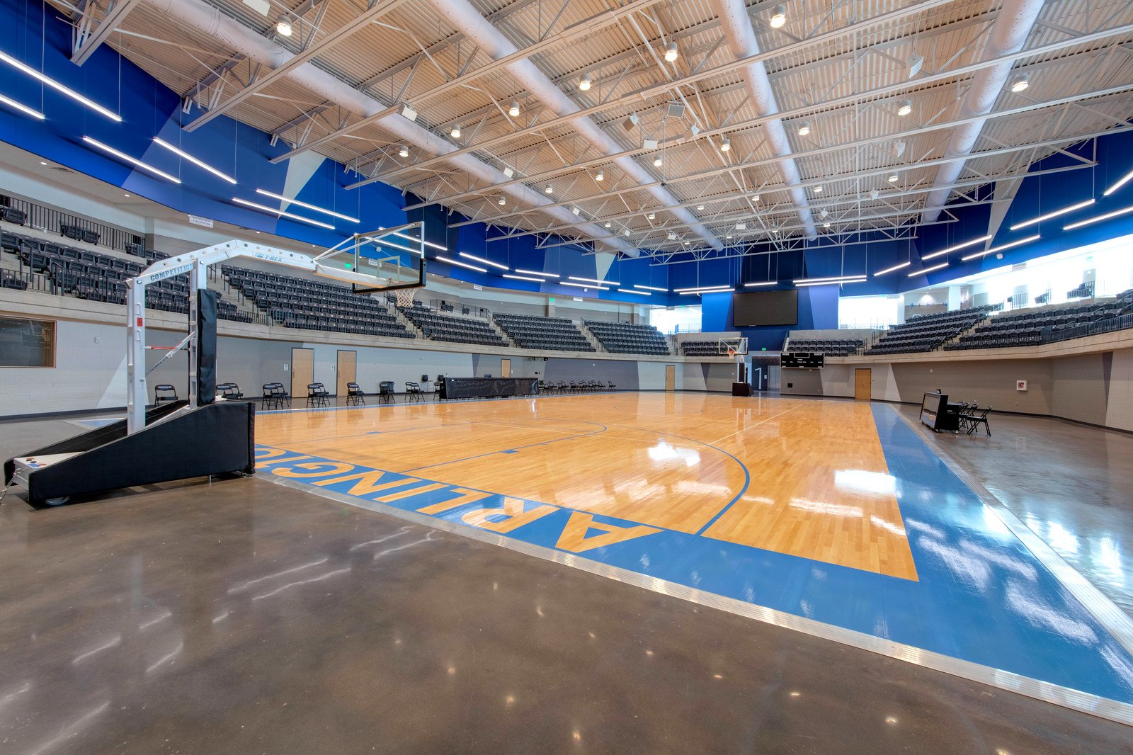 Empty indoor basketball court with seating and a large screen.
