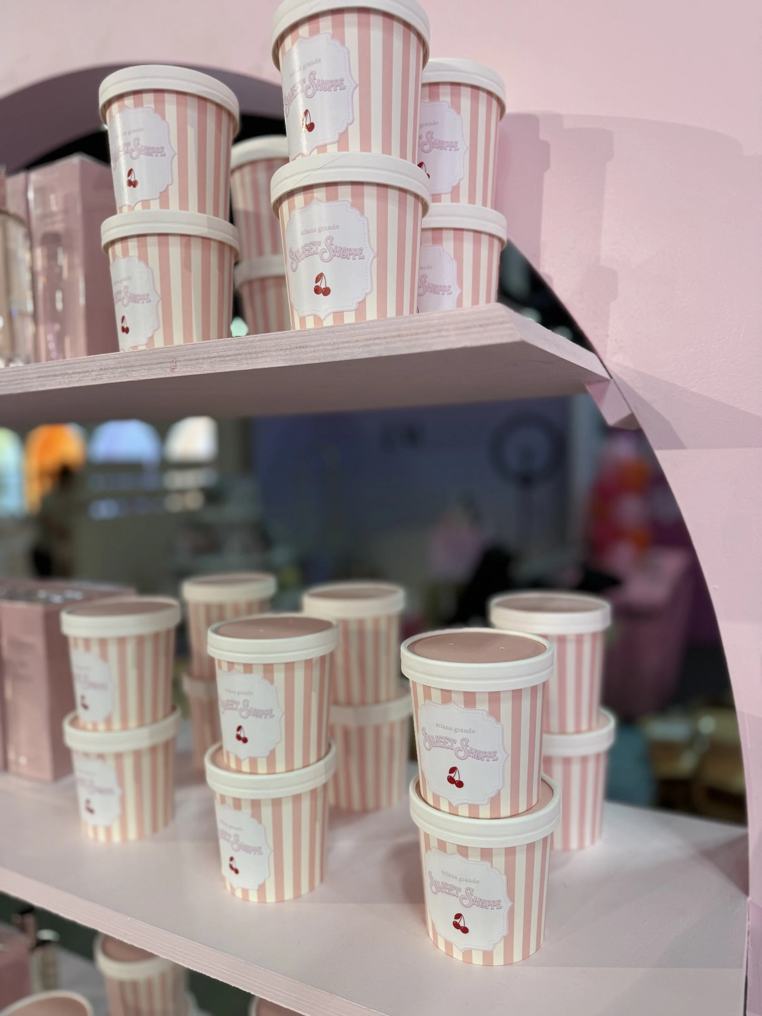 Pink striped containers with white lids and a label that says "Sweet Shoppe" with cherry illustrations, stacked on pink shelves.