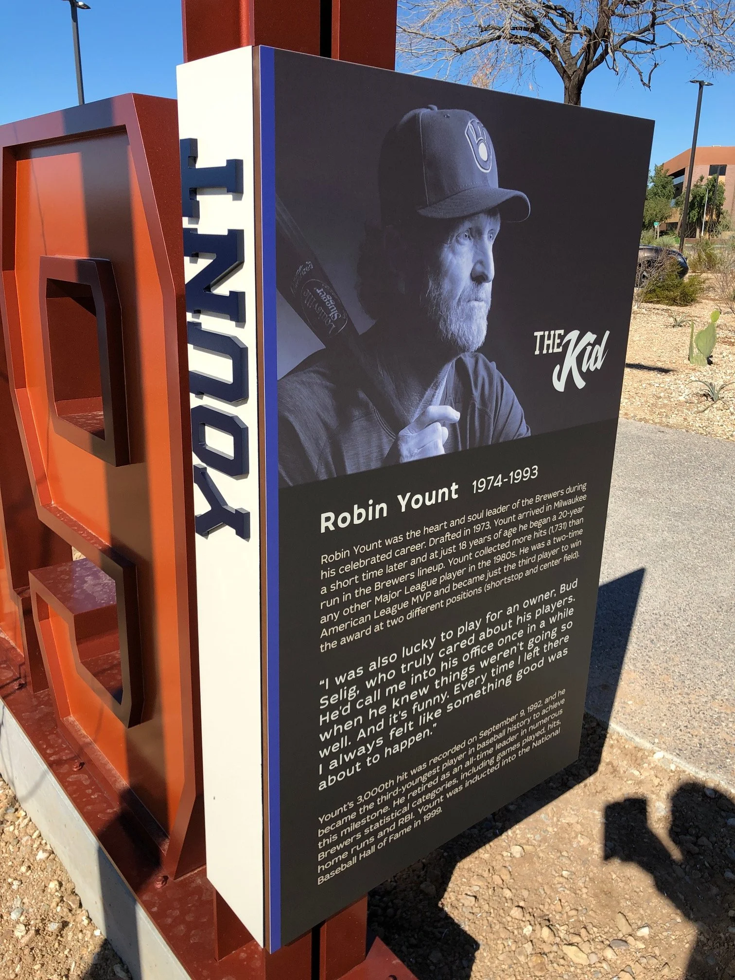 A memorial sign for Robin Yount located outdoors on a sunny day, featuring a black-and-white photograph of Robin Yount with a baseball bat, and text about his career and achievements for the MLB Milwaukee Brewers.