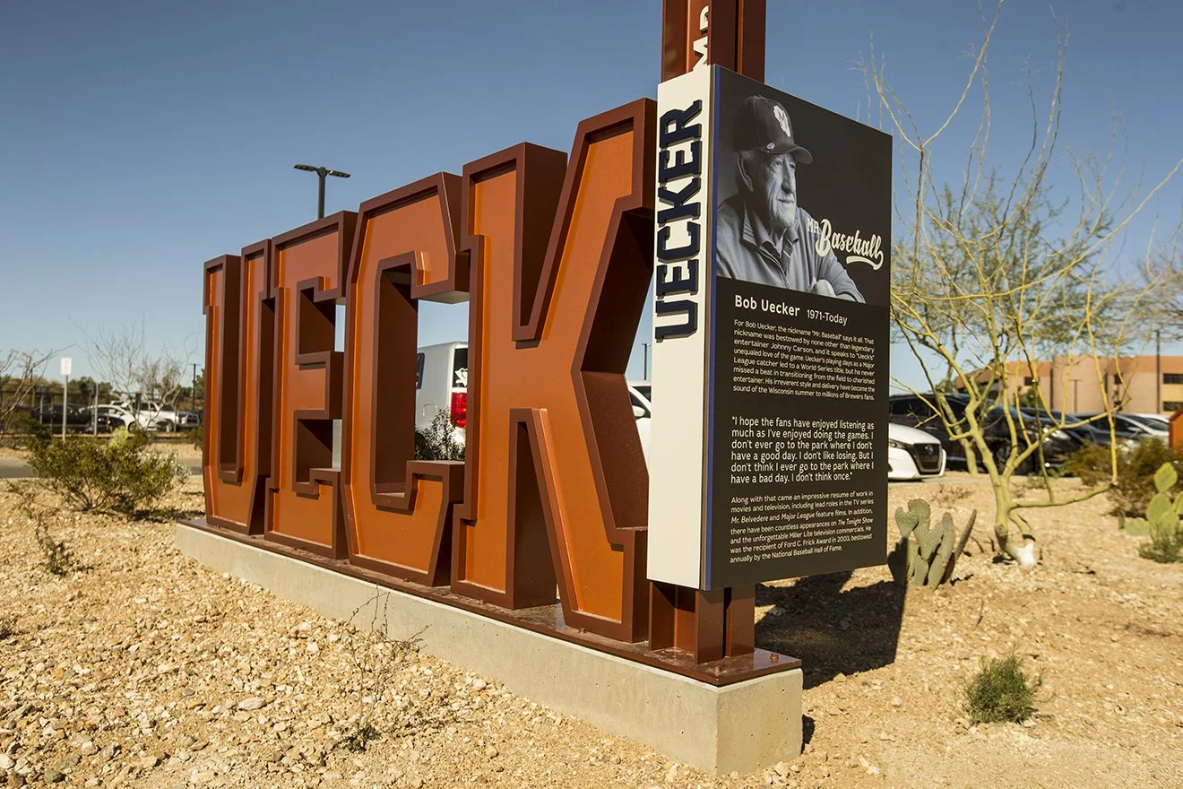 Large desert-style sign spelling out 'UECK' for Bob Uecker, past MLB commentator with a black and white photo of Bob Uecker and a description about his baseball career and achievements.