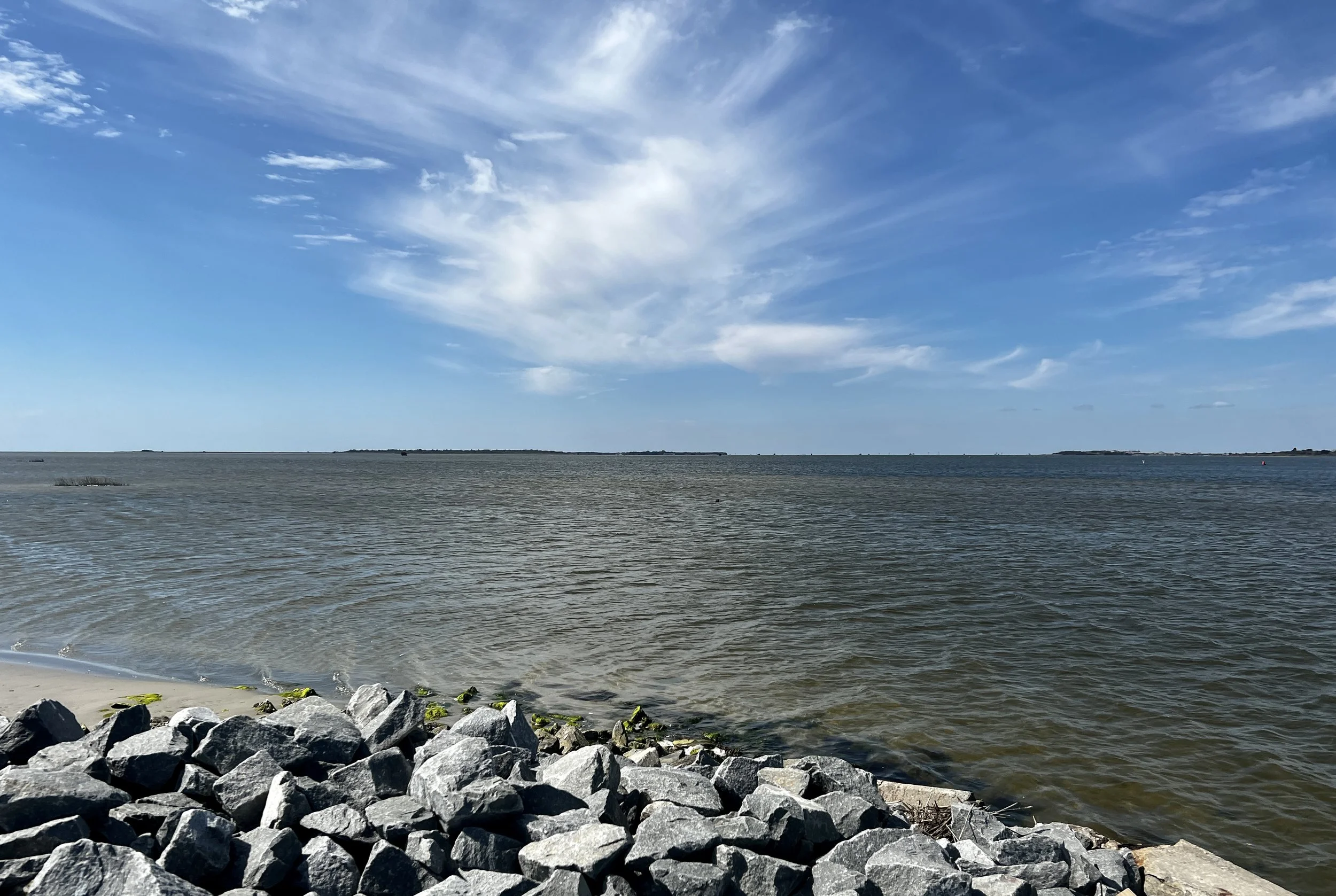 A rocky shoreline with a calm body of water and a partly cloudy blue sky.