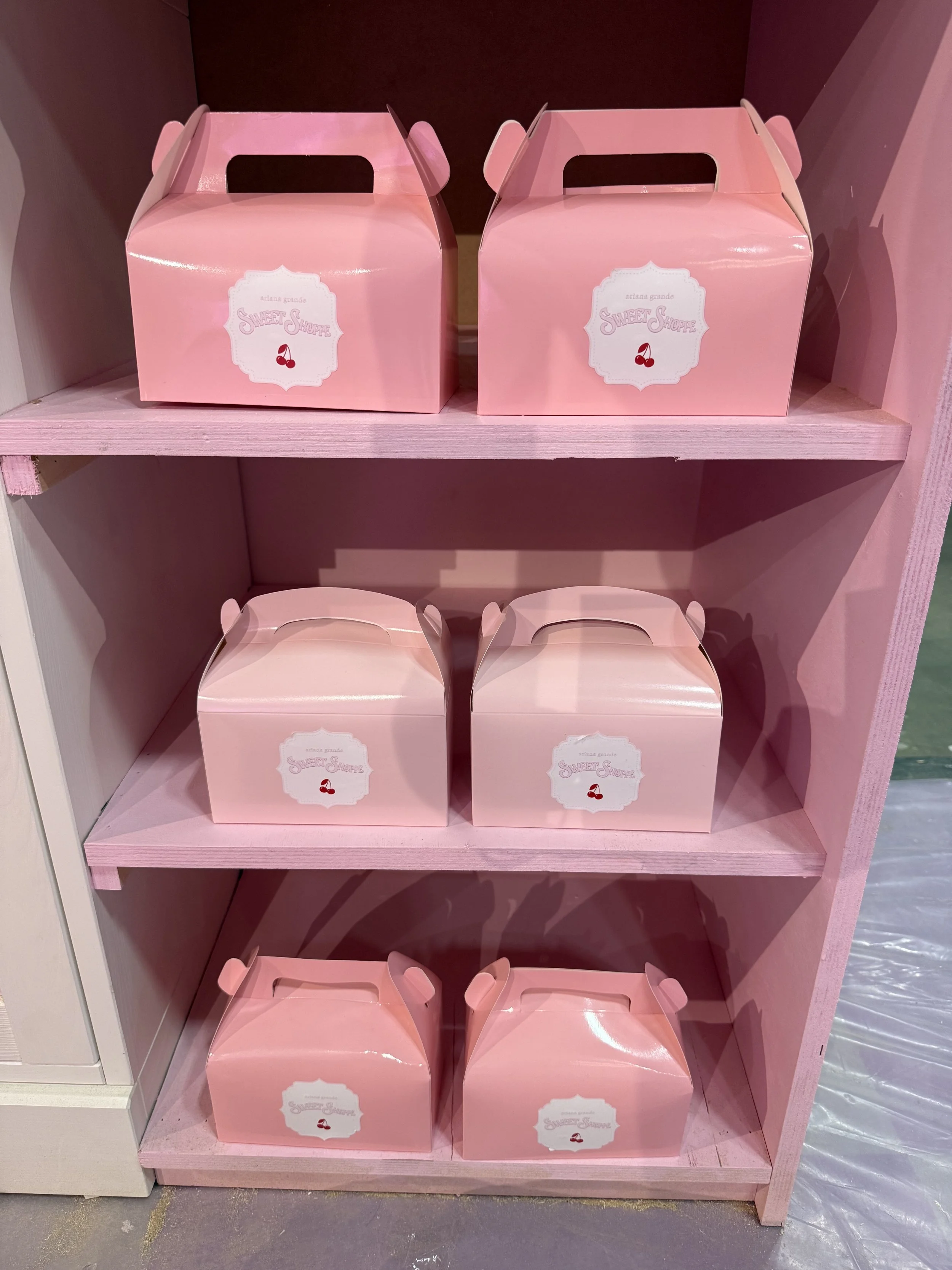 Six pink boxes with handles on a pink wooden shelf, labeled with 'Sweet Shoppe' and cherry graphics.