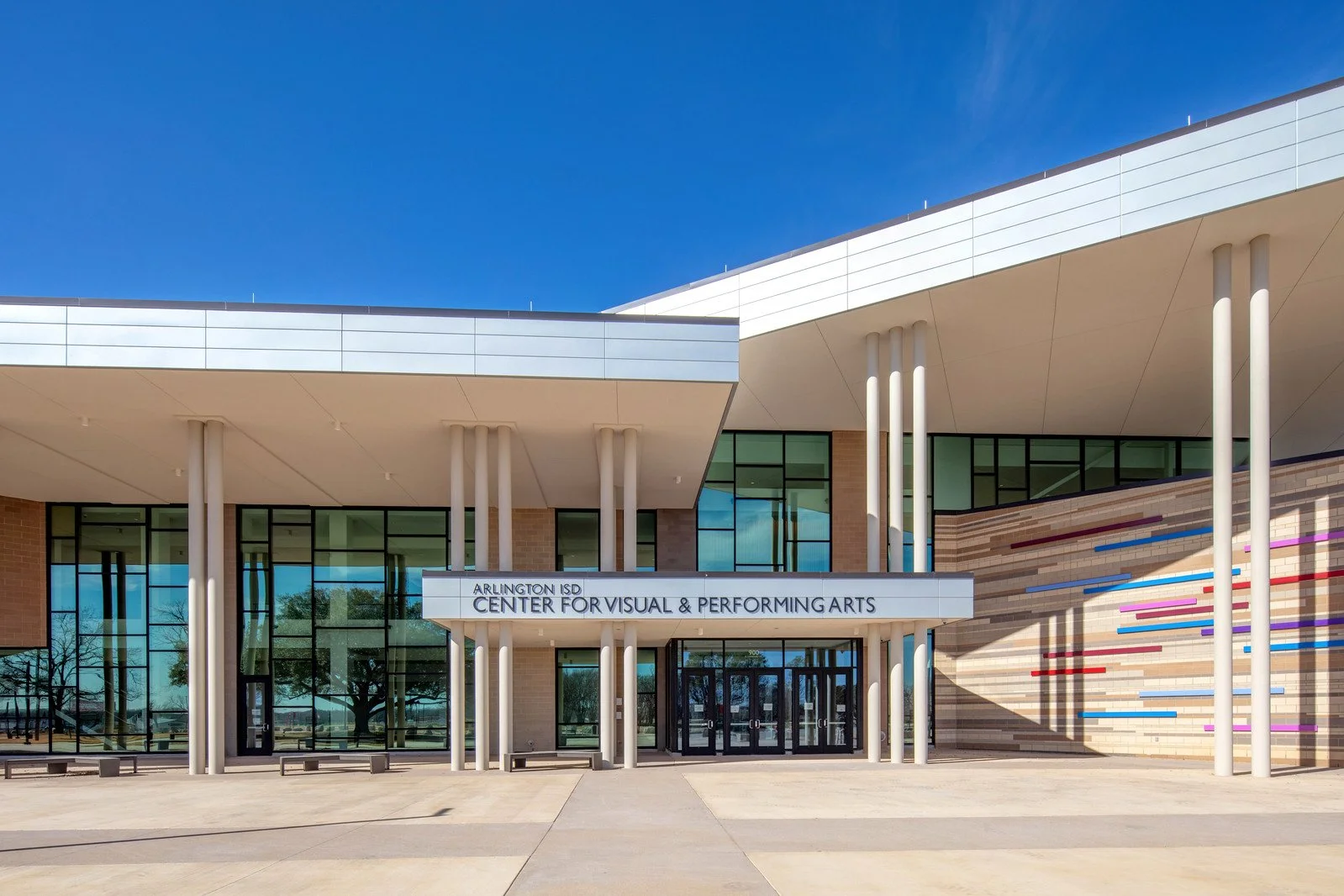 Front view of Arlington ISD Center for Visual & Performing Arts building with glass windows, modern architecture, and colorful line design on the wall, under a clear blue sky.