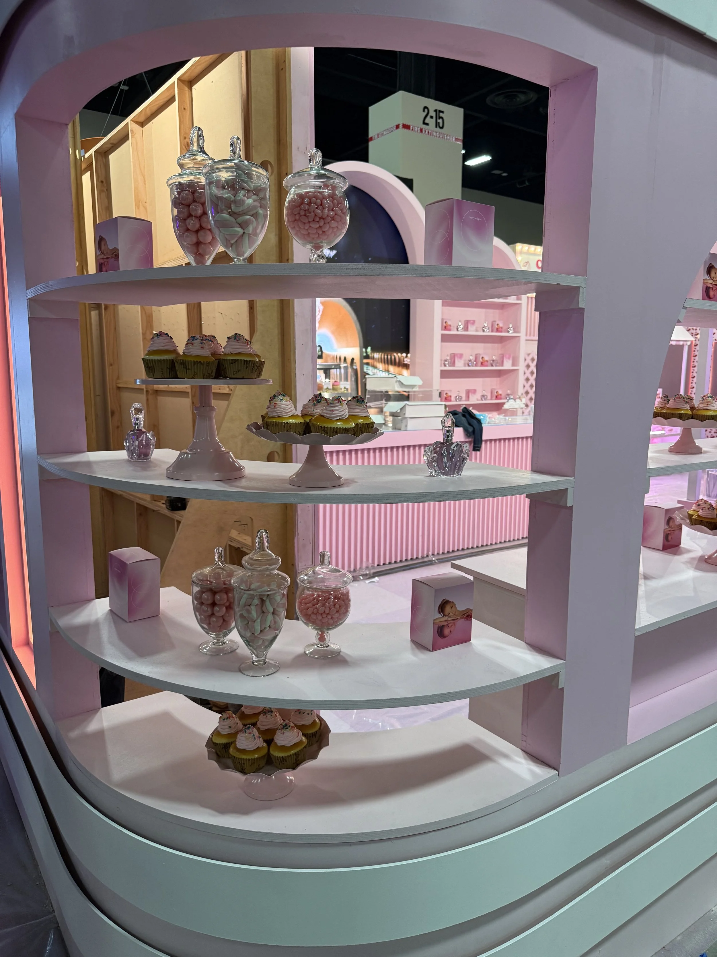 Display of pink and white candy, cupcakes with pink icing, and decorative jars with pink candies in a pink-themed store or bakery for the Ulta Beauty World expo in Las Vegas. 