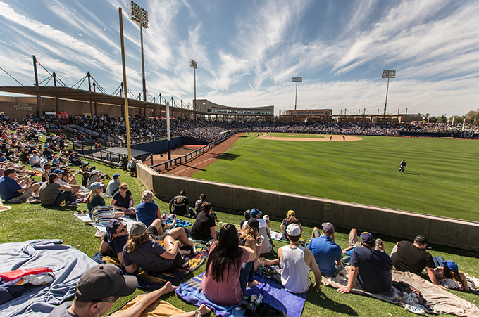 Spectators sitting on blankets and chairs watching an MLB pre season spring training baseball game in a stadium with a partly cloudy sky.