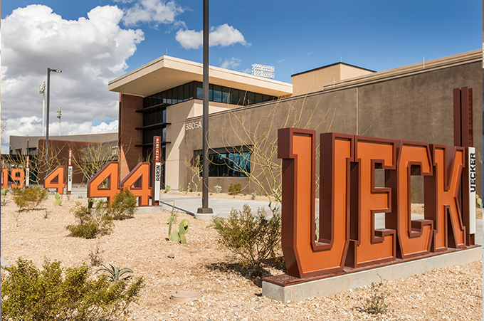 Outdoor view of a modern building with large orange letters spelling 'UECK' and other number signs in desert landscaping at the MLB Milwaukee Brewers Spring Training facility in Phoenix, Arizona.