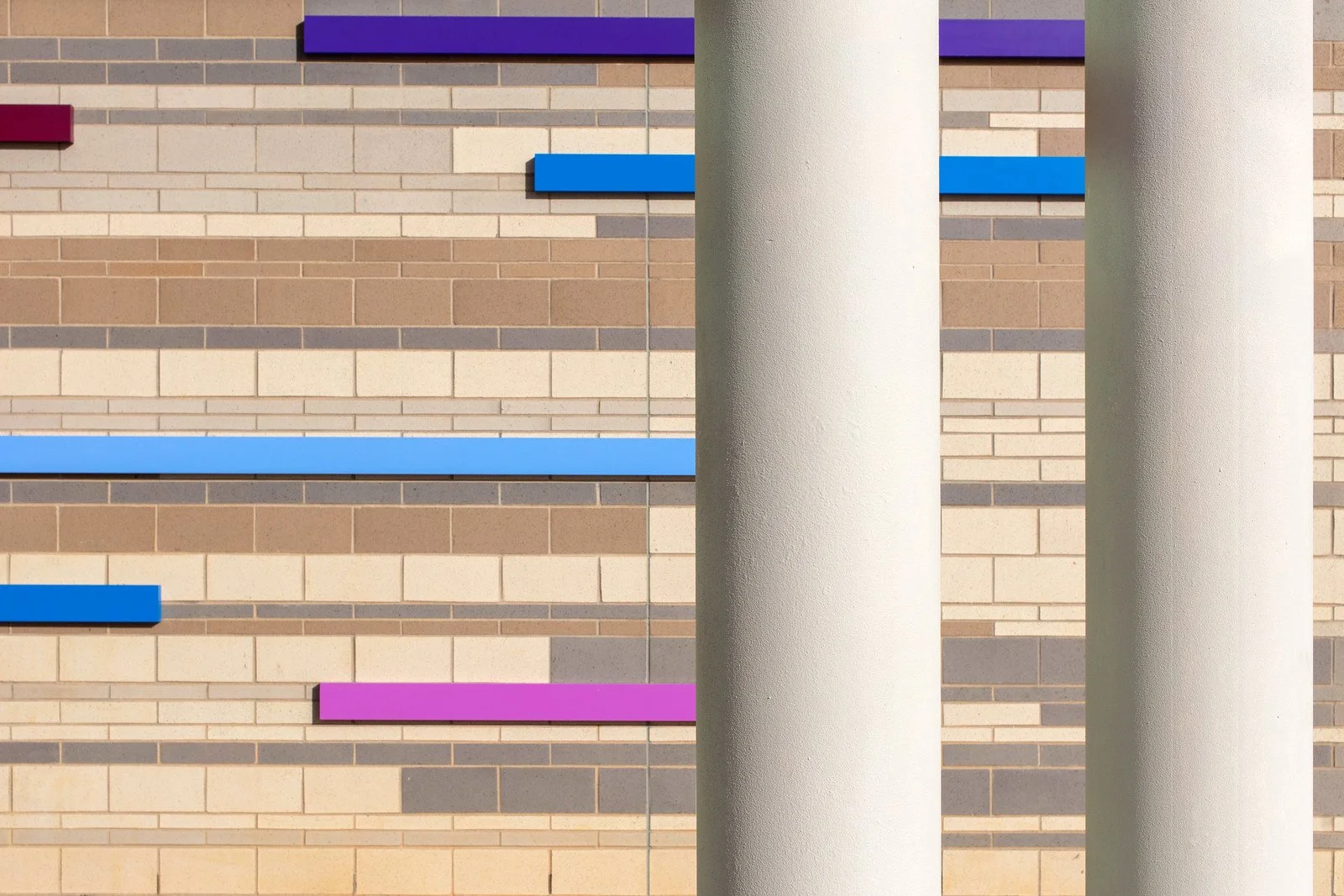 Close-up of a brick wall with colorful horizontal bars and two white vertical columns.
