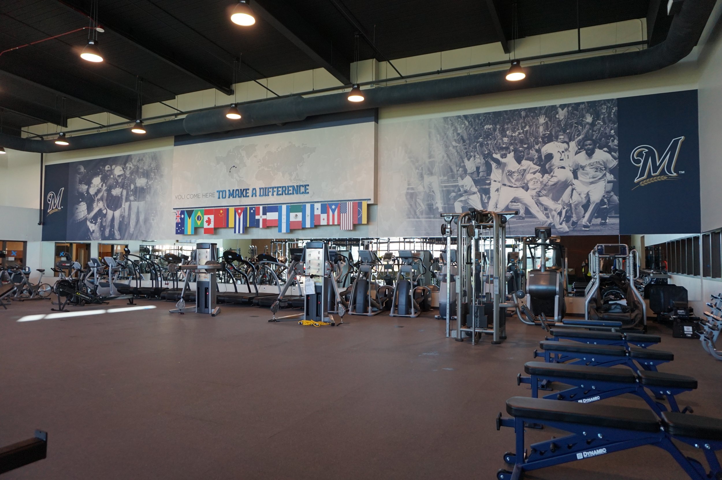 Large gym with exercise equipment, banners, and large black-and-white sports photos on the walls for the MLB Milwaukee Brewers.