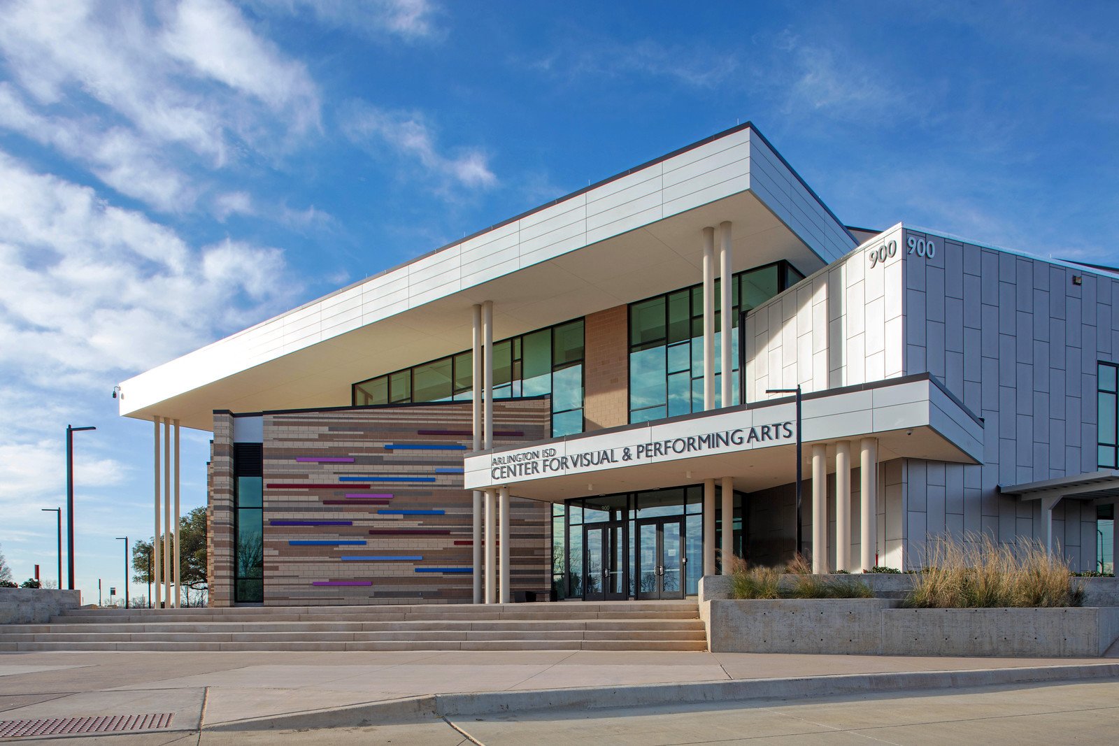 Modern arts center building with glass windows, white and gray exterior, and colorful horizontal decorative elements on a sunny day.