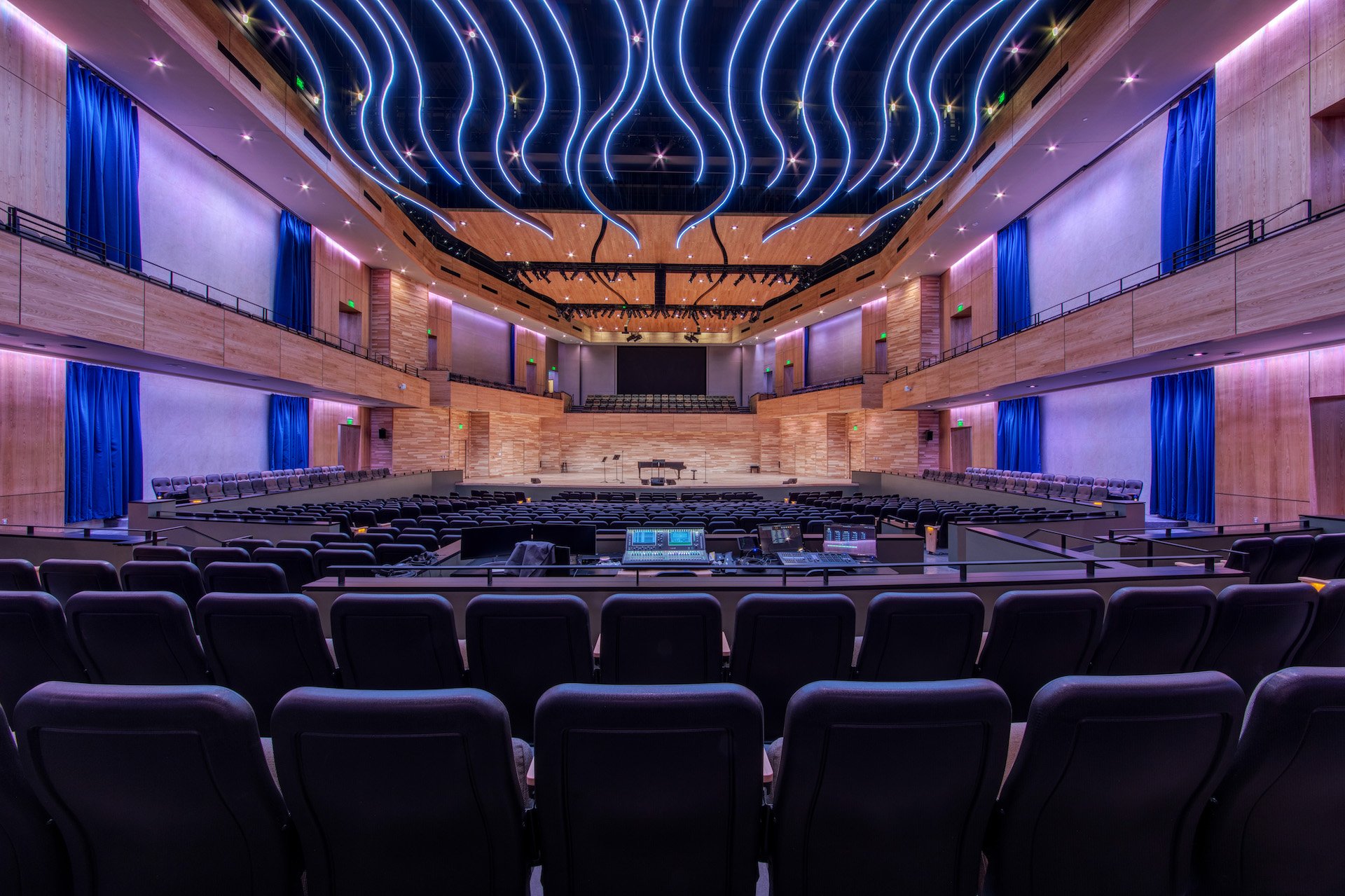 A large, modern auditorium with a wooden stage, rows of seating, and colorful lighting on the ceiling.