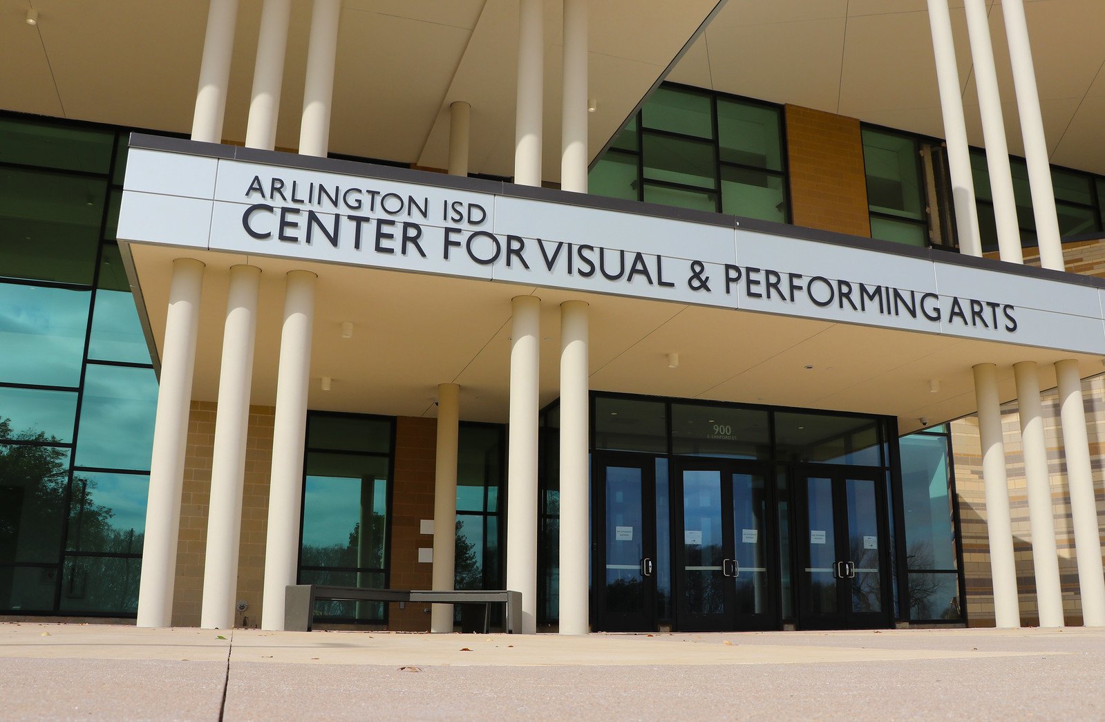 Exterior view of the Arlington ISD Center for Visual & Performing Arts building with a sign, glass windows, and white pillars.