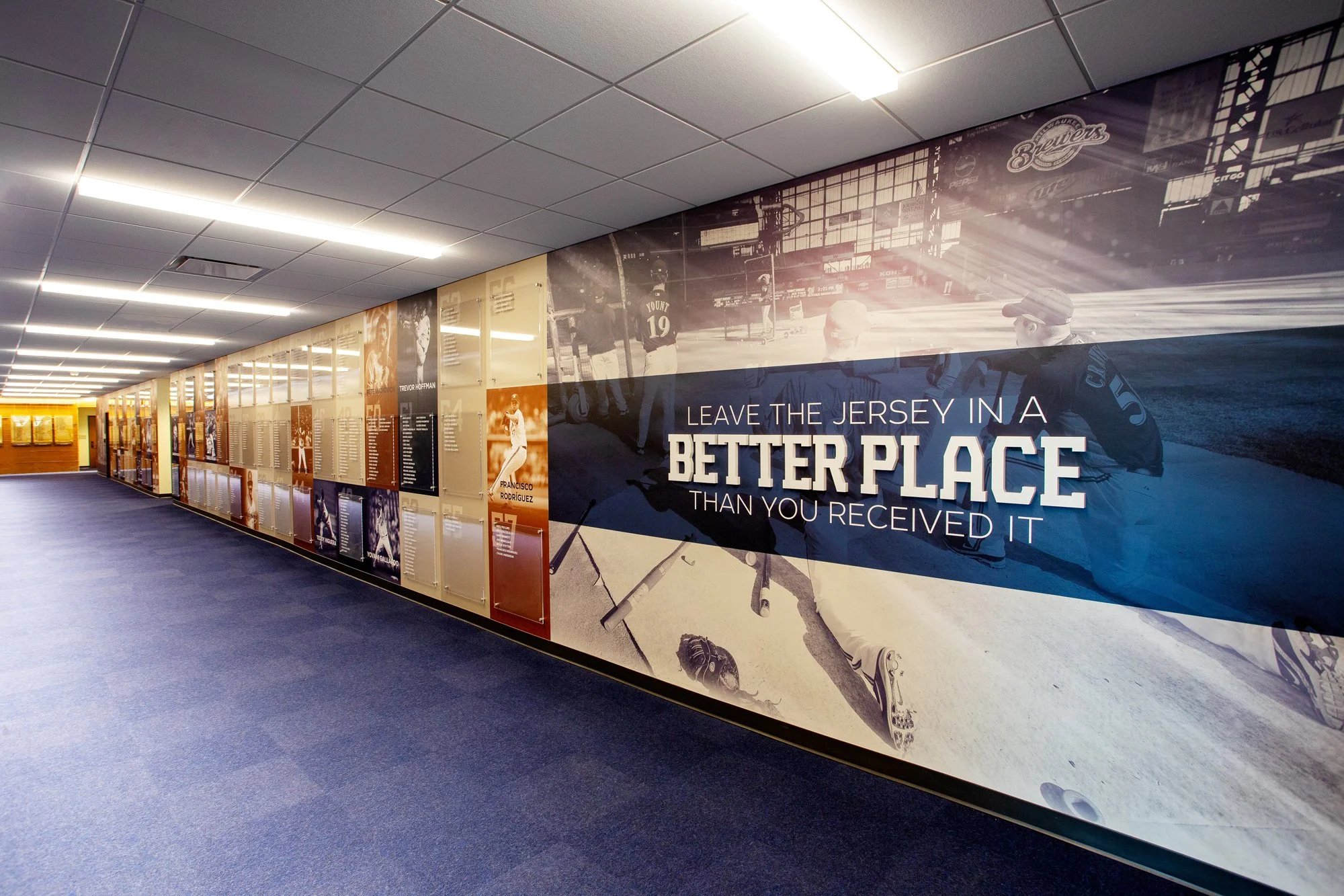 A hallway with a mural on the wall featuring a sports message that says, 'Leave the jersey in a better place than you received it,' with images of athletes and sports scenes for the MLB Milwaukee Brewers.