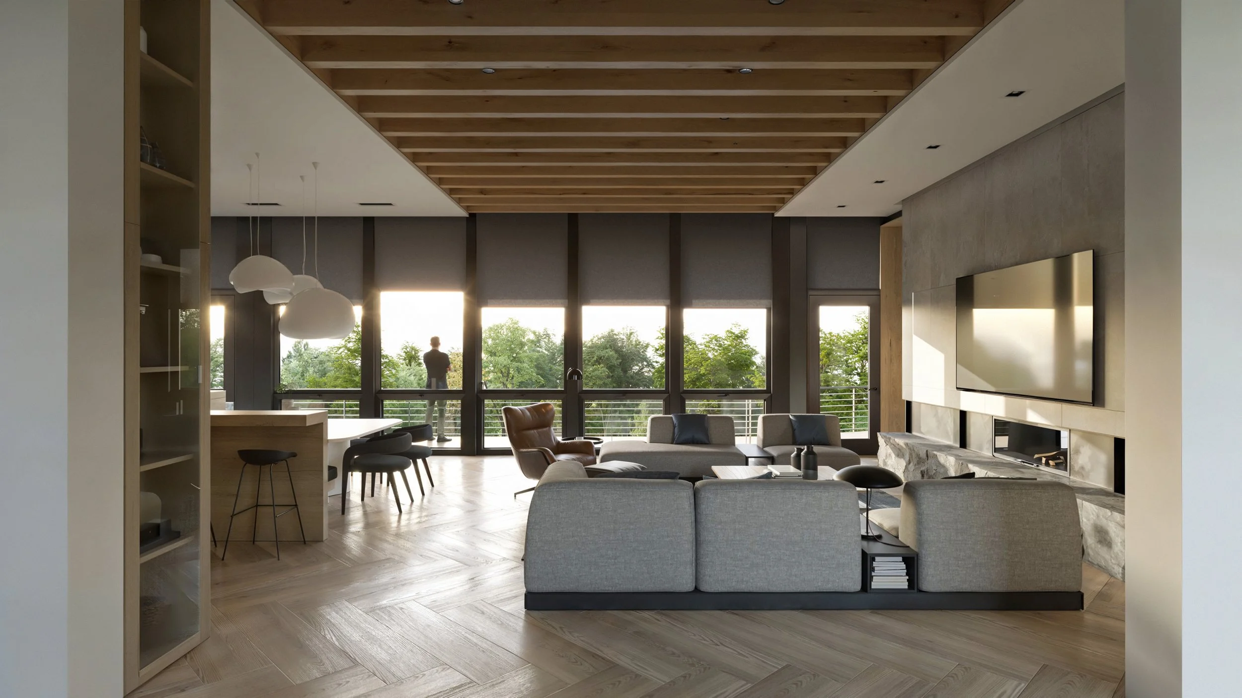 Modern living room with large windows, gray sofas, a stone fireplace, and a mounted flat-screen TV, with a man standing outside on a balcony visible through the windows.