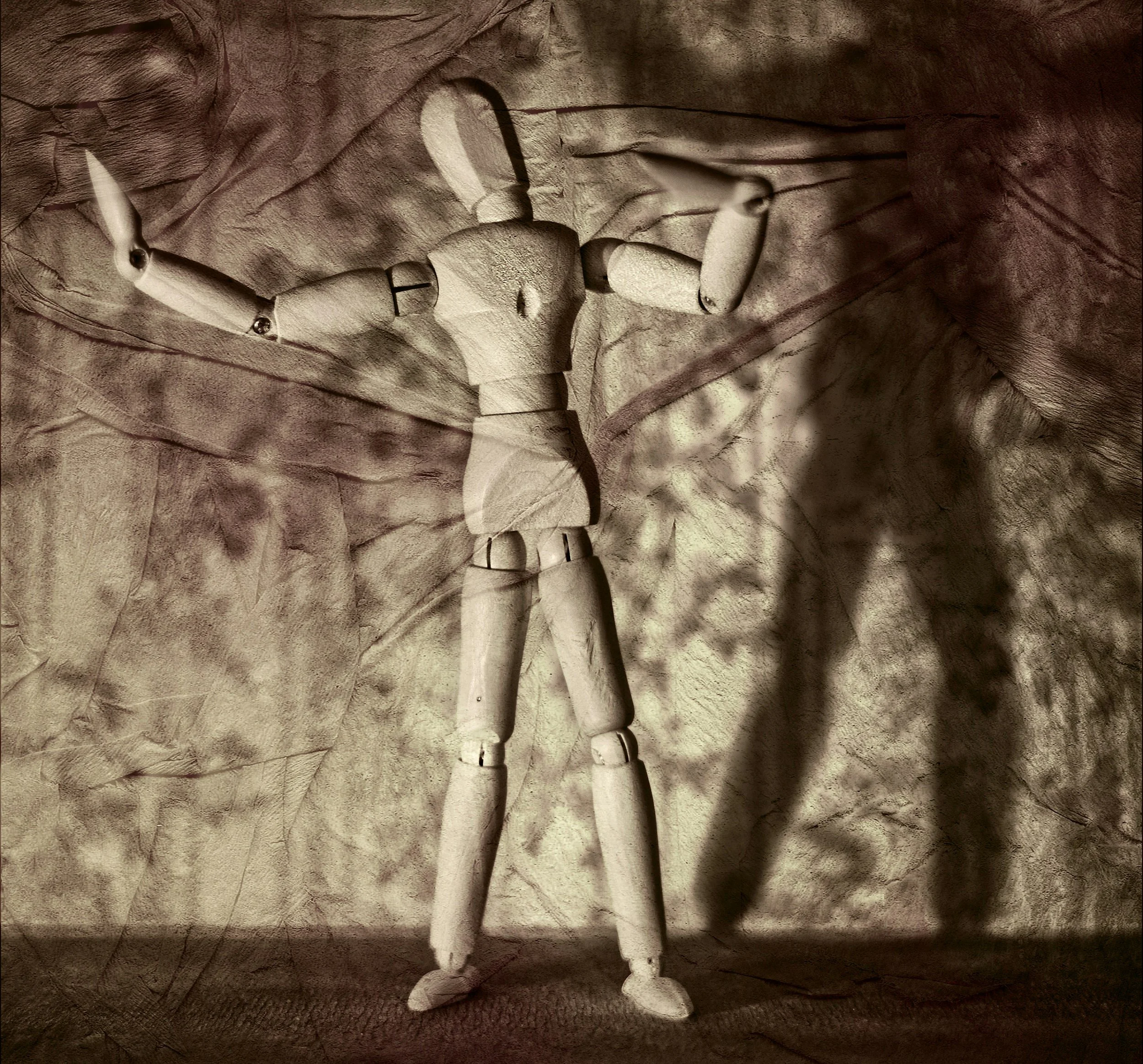 A wooden sculpture of a humanoid figure with a distorted face, elongated limbs, carvings, and bolts, situated on a wooden surface.