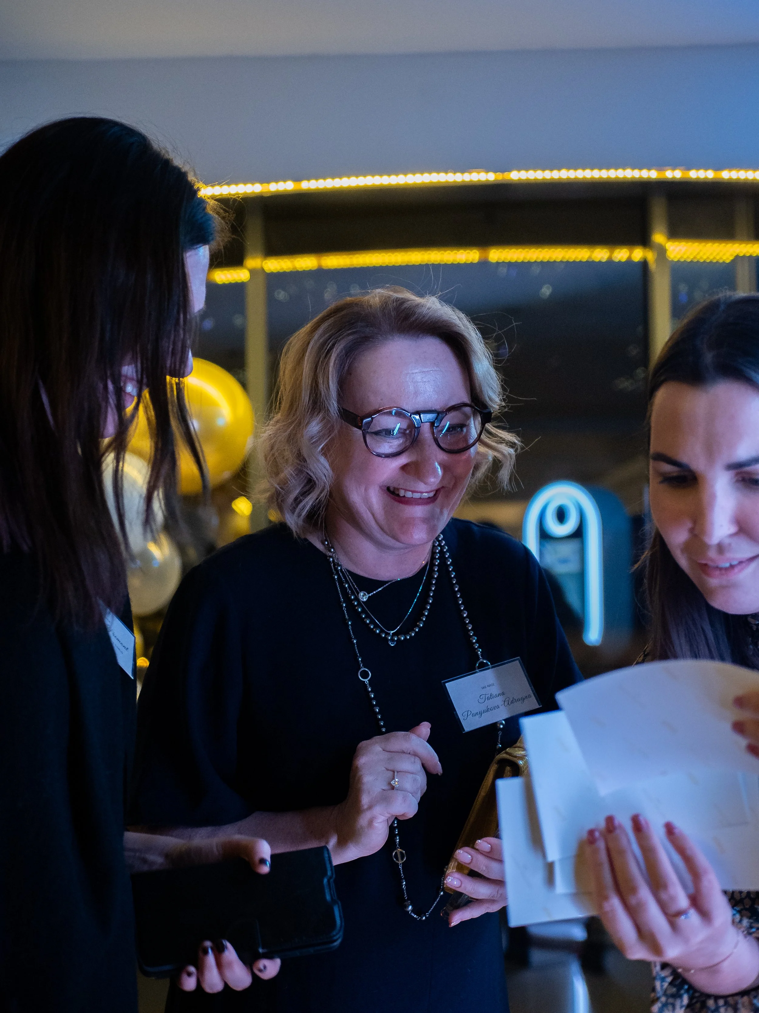 Trois femmes souriantes regardant un cadeau dans une ambiance festive.