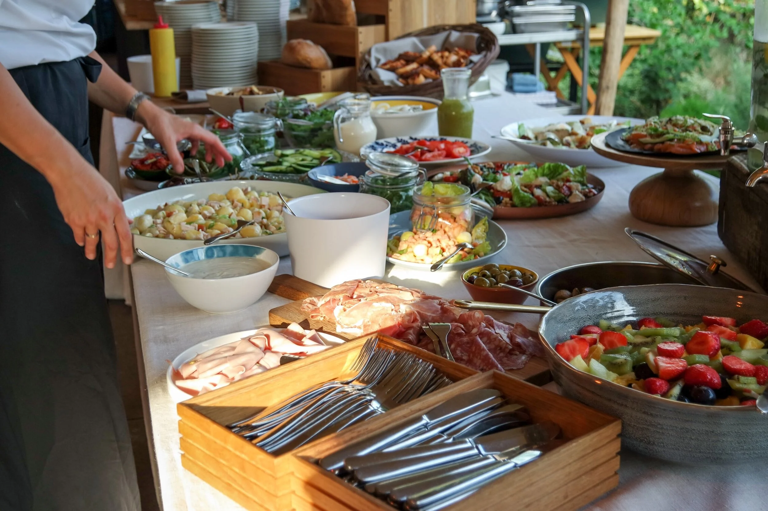 Buffébord med olika sallader, grönsaker, bröd och pålägg vid ett utomhusarrangemang.