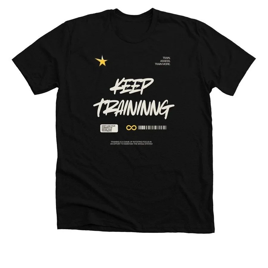 Black T-shirt with bold white text that says 'KEEP TRAINING'. Additional smaller text includes 'TRAIN. ASSESS. TRAIN MORE.' and motivational phrases. Gold star and barcode graphics are also present.