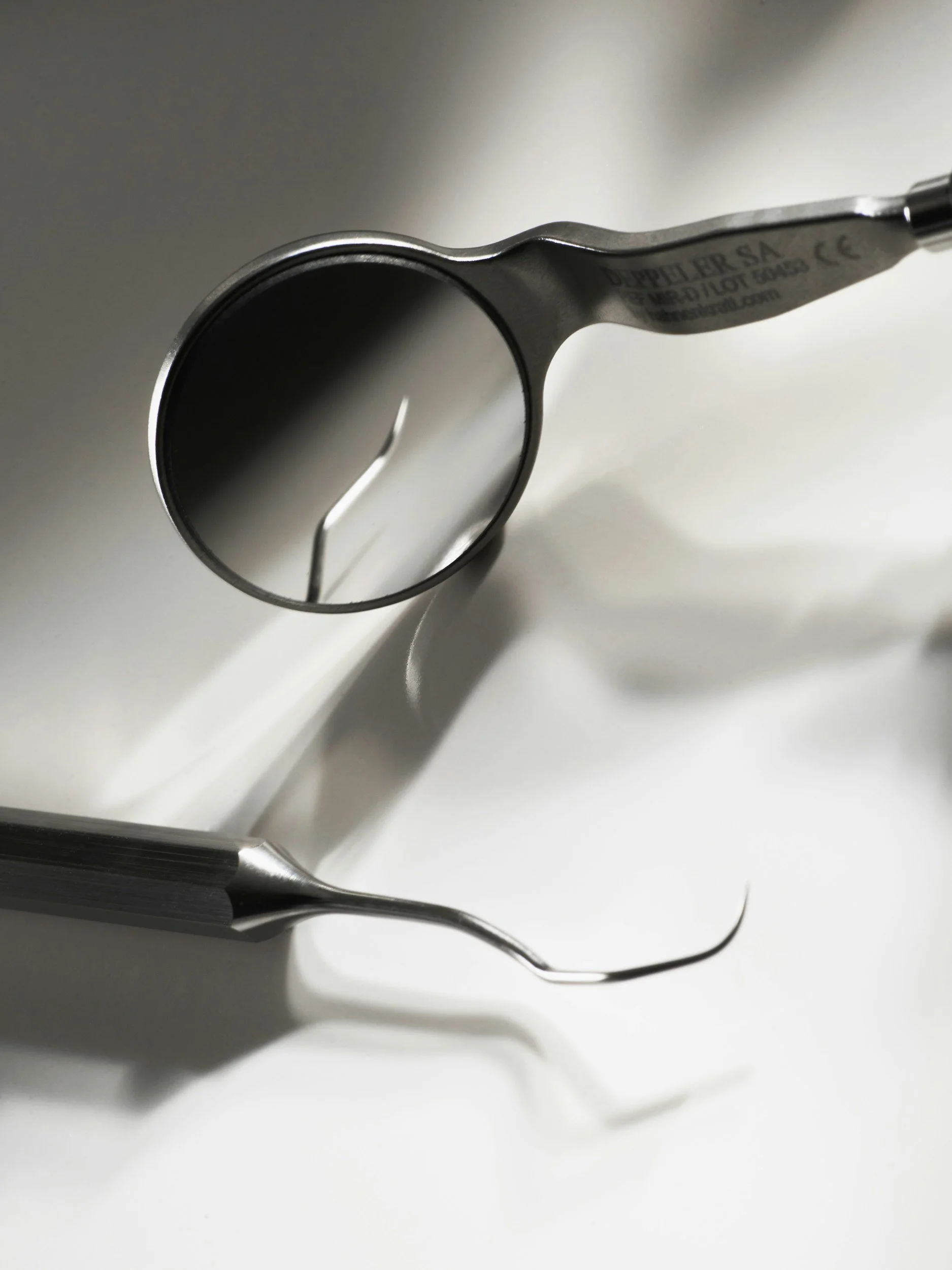 Close-up of a dental dental mirror on a white surface, with a reflection visible in the mirror.