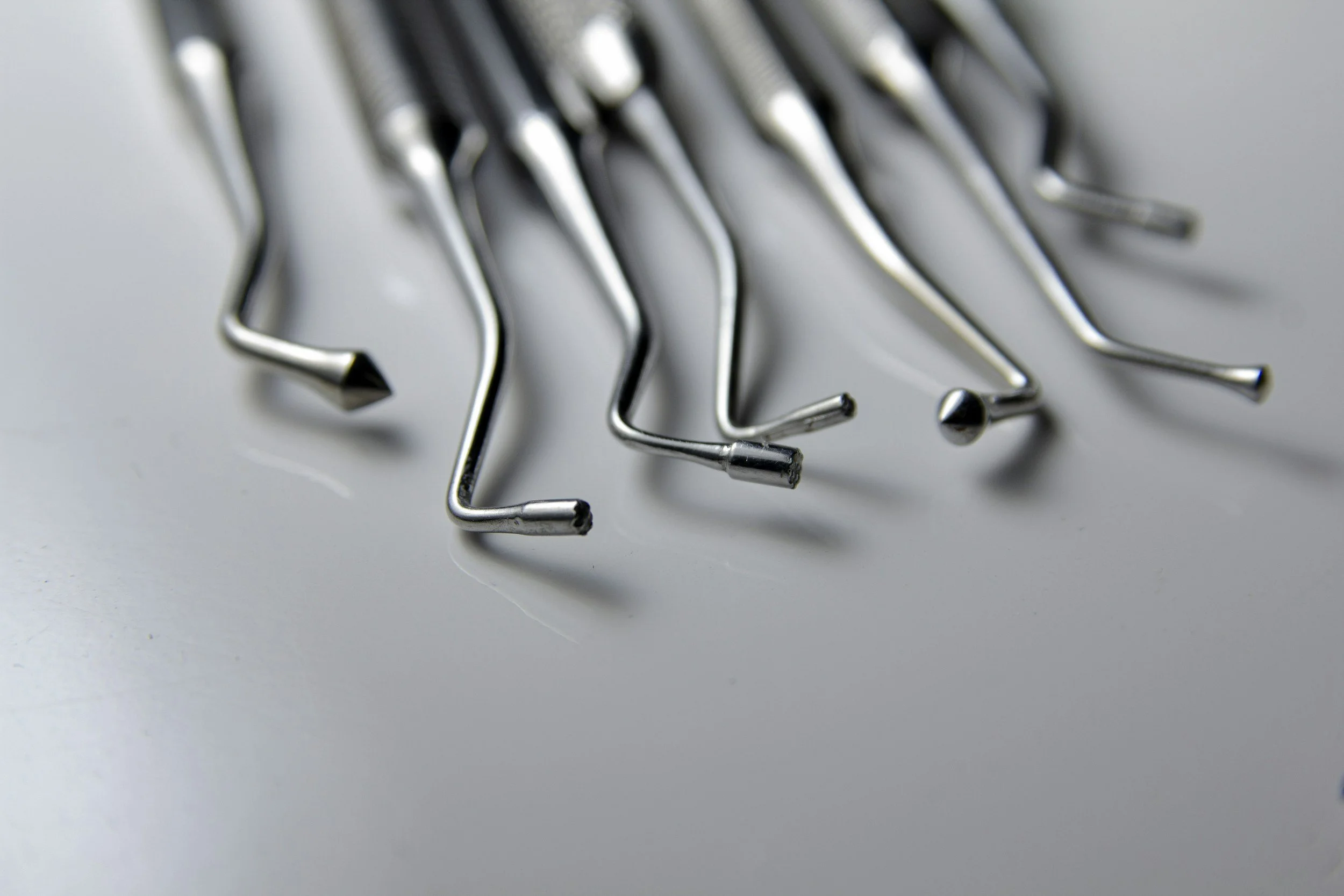Close-up of several stainless steel dental or surgical tools arranged on a white surface.