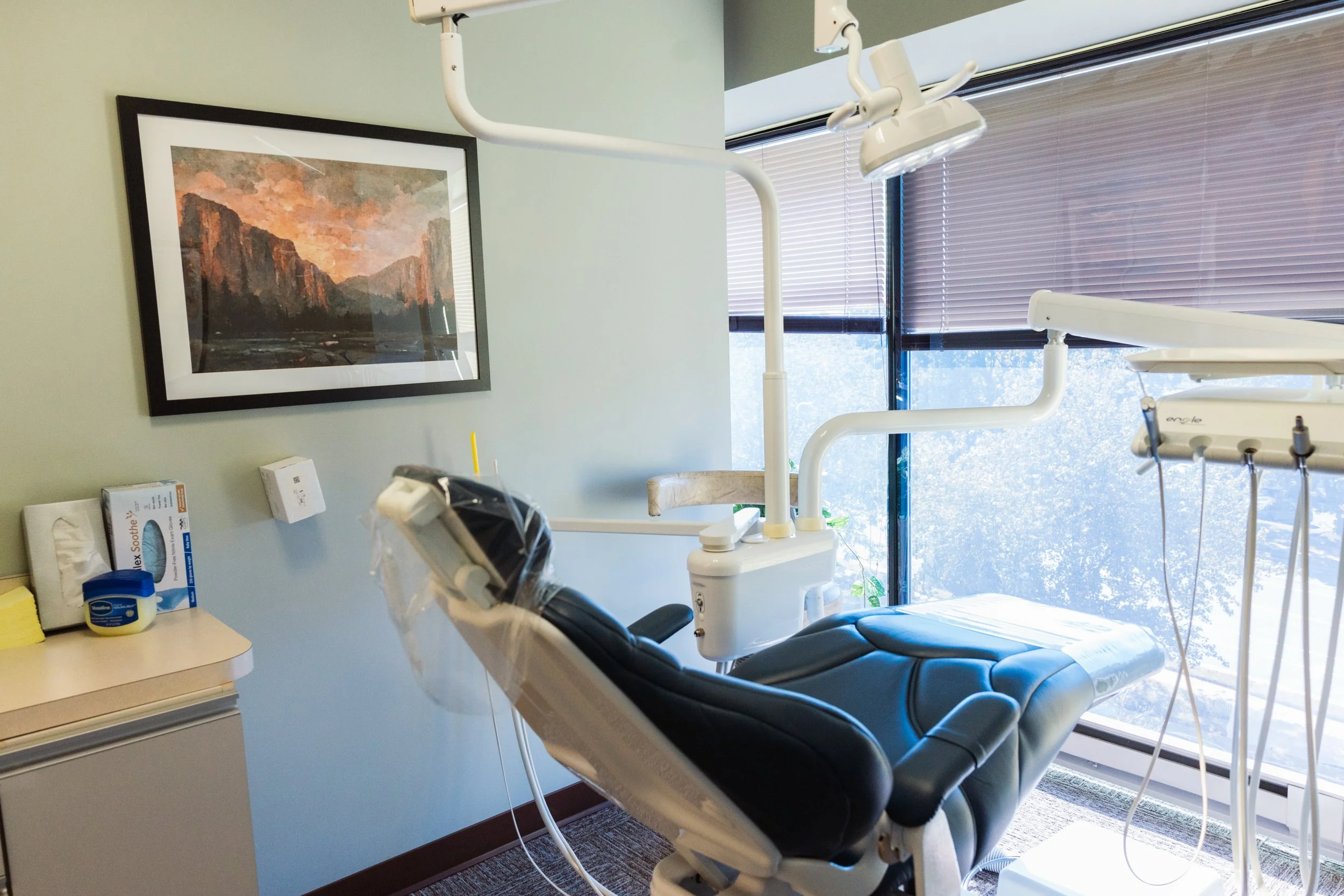 Dental operatory with a blue chair and large windows in front.