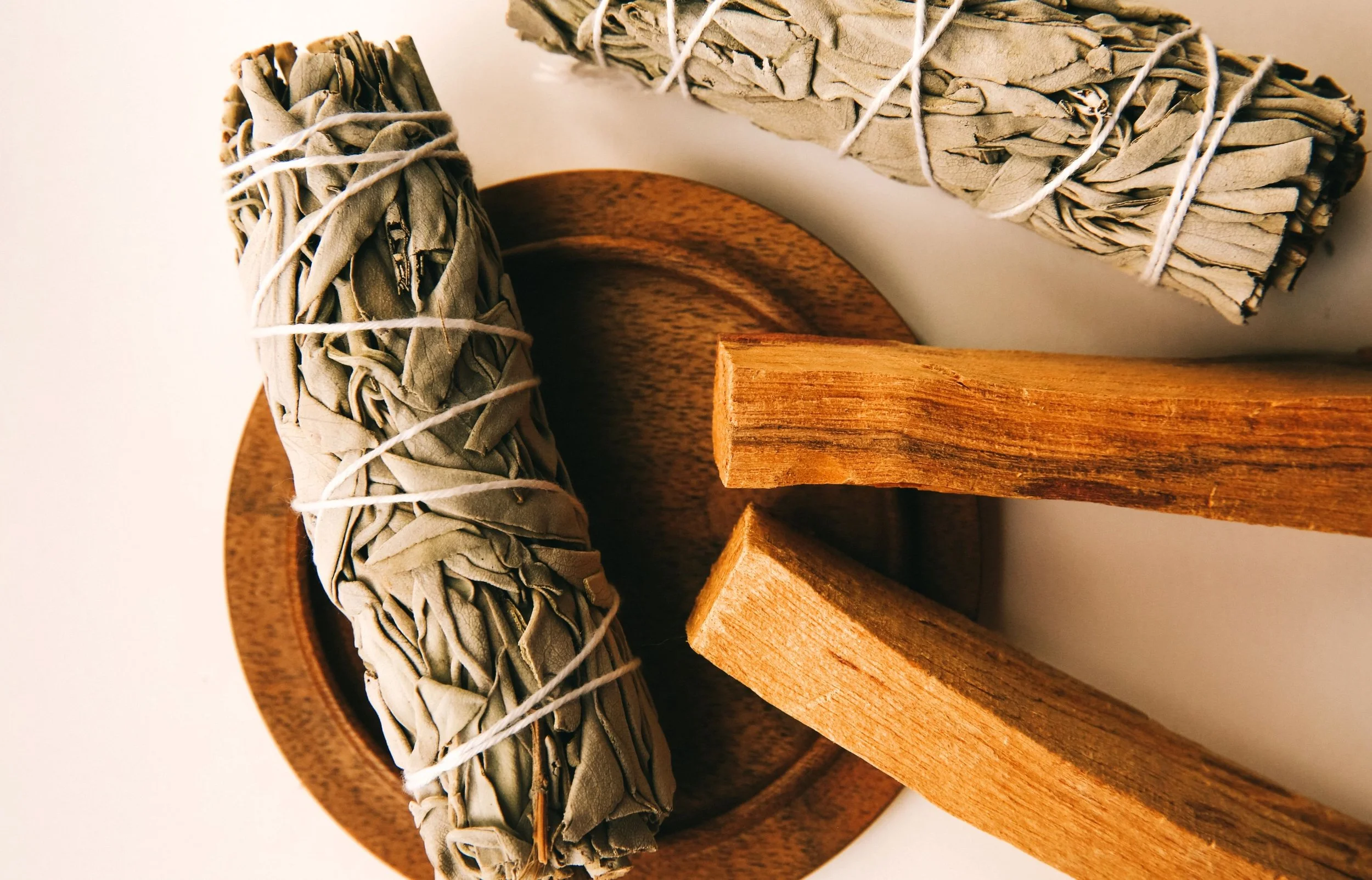 Bundles of dried sage and palo santo sticks placed on a wooden surface.
