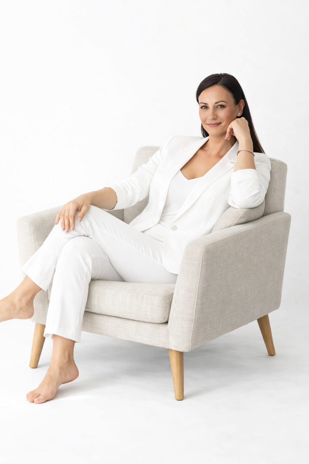Woman in white suit sitting in a gray armchair on a white background.