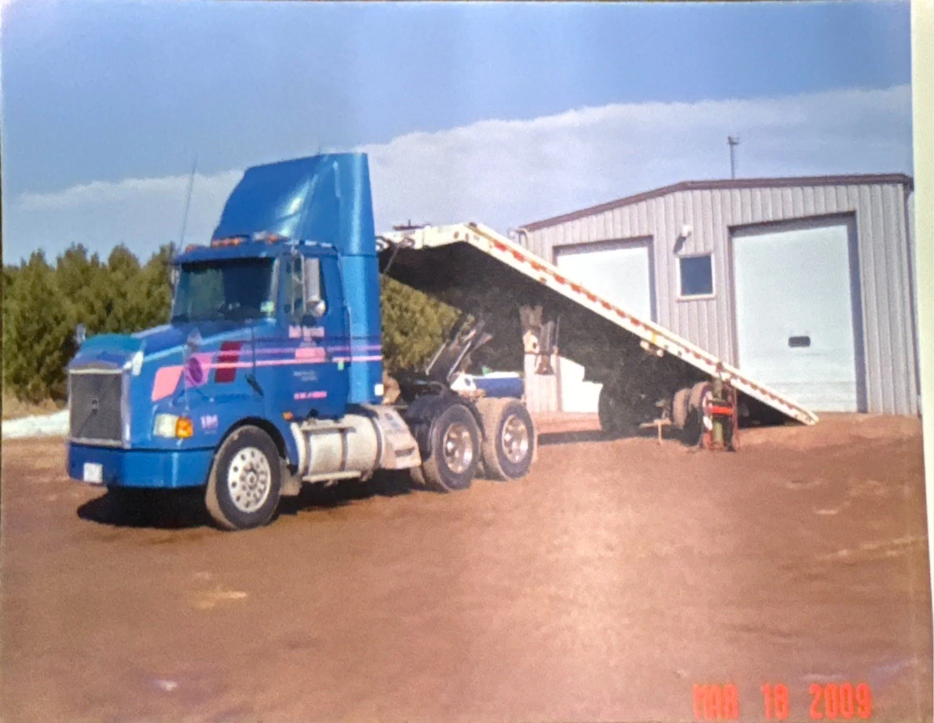 Blue Volvo semi-truck with a shipping container trailer fully extended.
