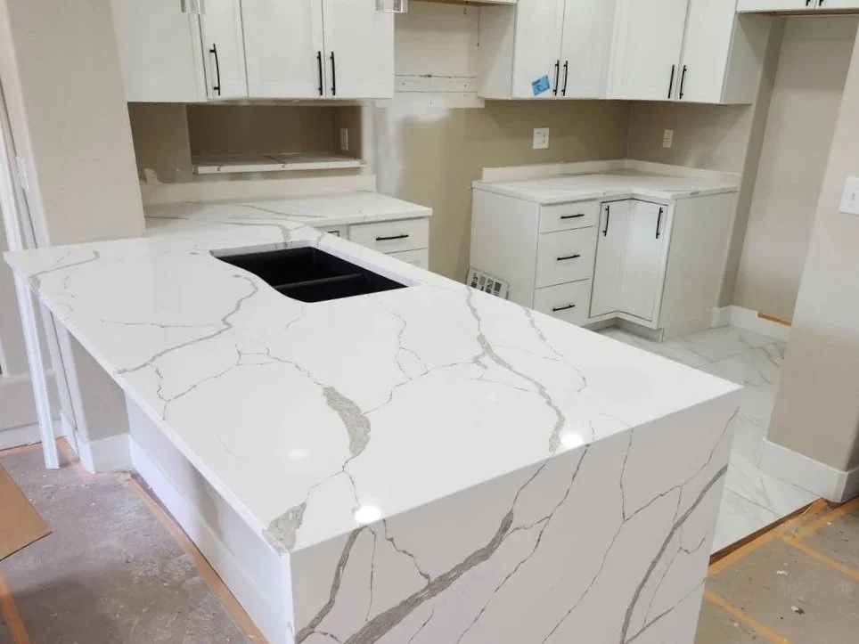 Kitchen with white marble countertops and cabinetry, black sink cutout, and partially installed appliances.