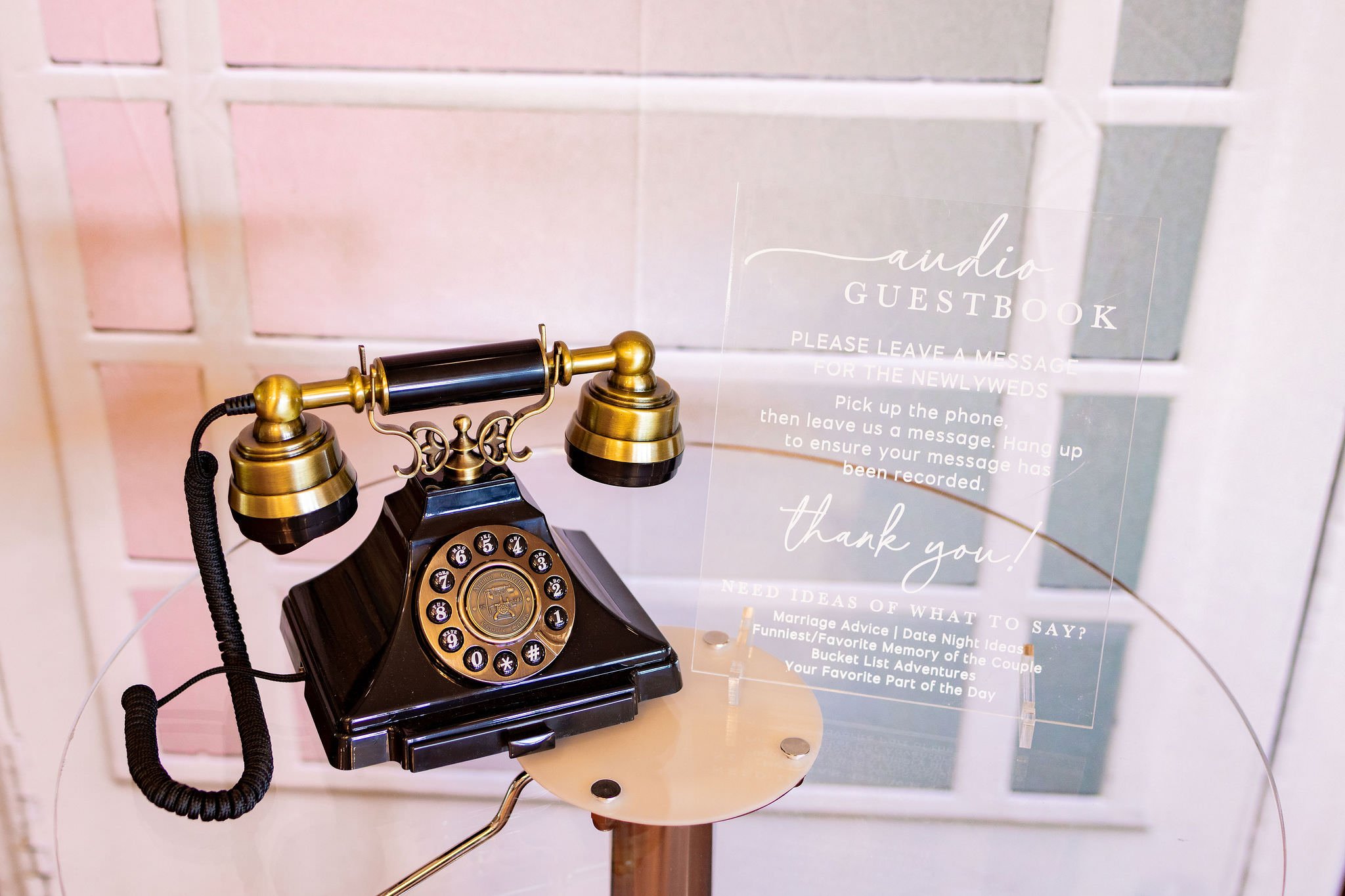 Vintage black and gold rotary telephone on a small round table with a transparent acrylic guestbook sign next to it.