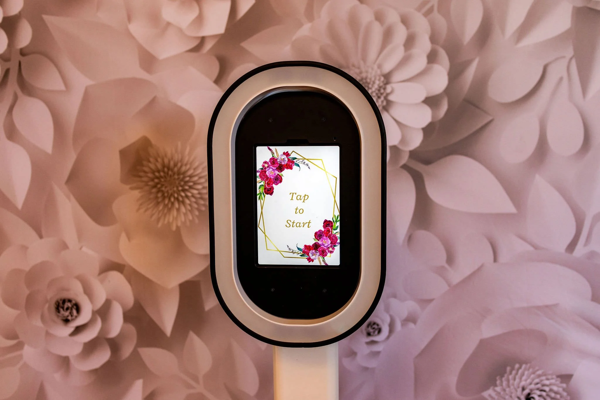 Touchscreen device with a floral welcome message on a pink floral wall background