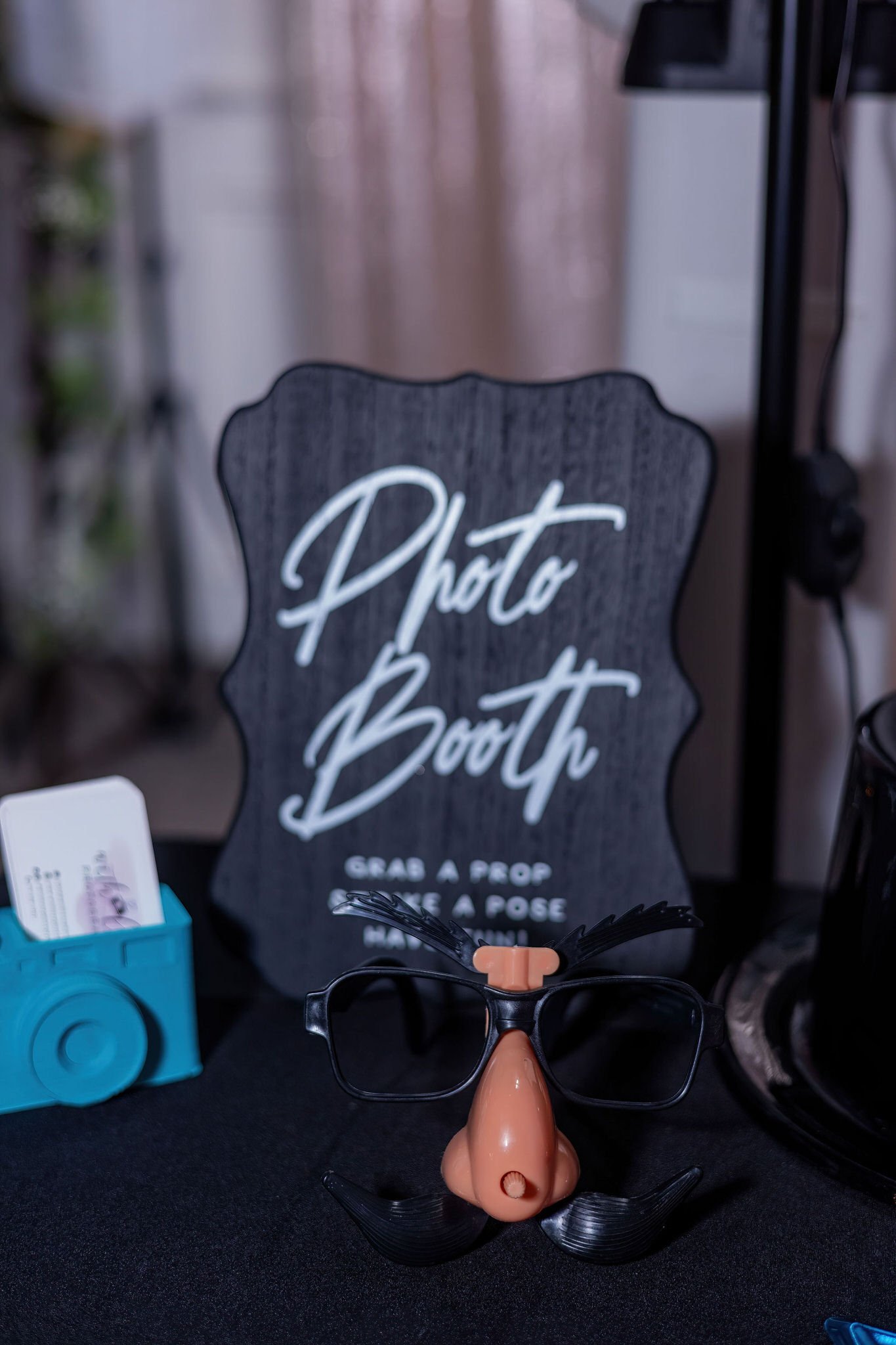 Photo booth setup with novelty glasses featuring a nose, mustache, and eyebrows, and a sign that reads 'Photo Booth' with instructions to grab a prop, take a pose, and have fun.