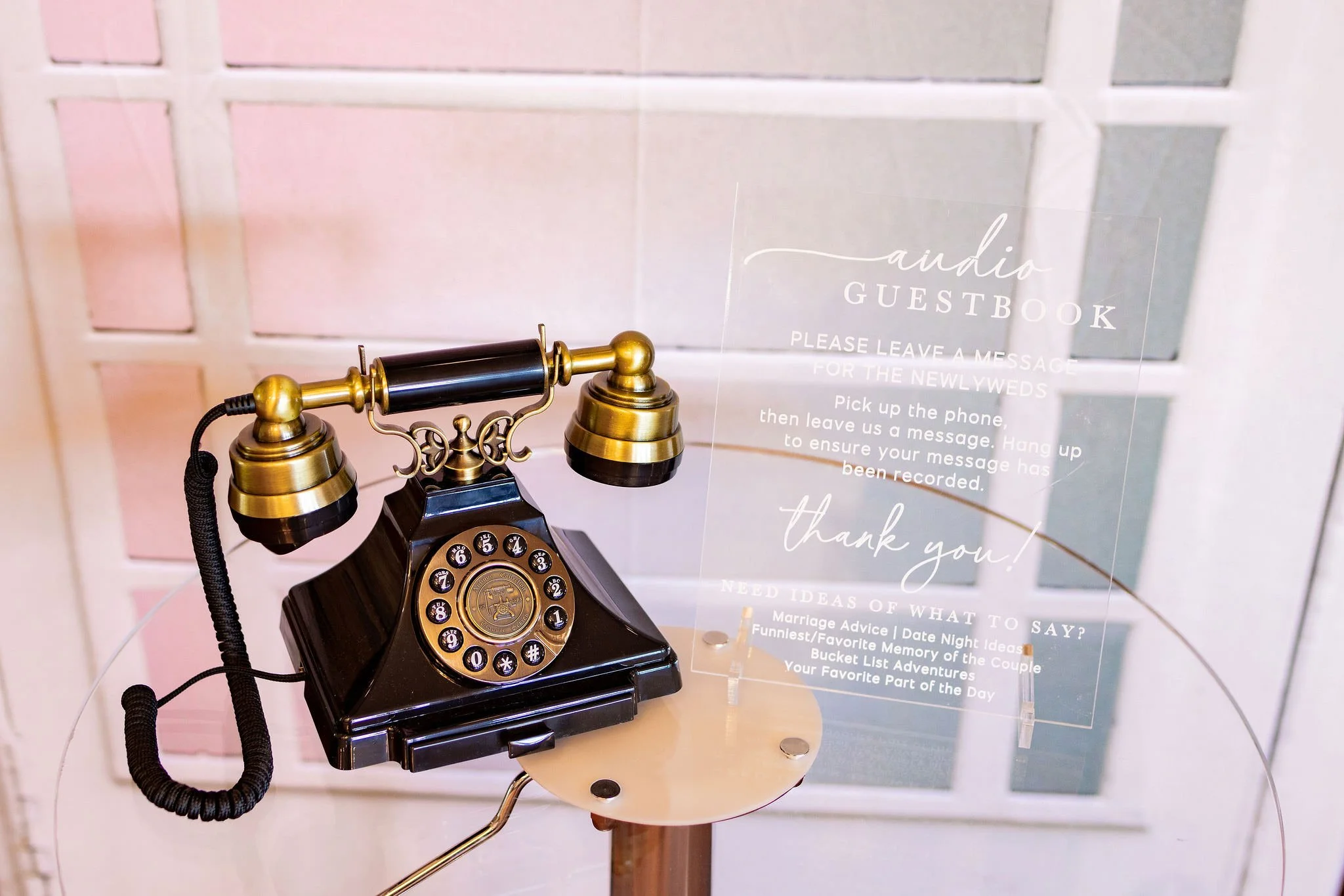 Vintage black and gold rotary phone on a wooden table, with a clear acrylic sign about a guestbook and message instructions.