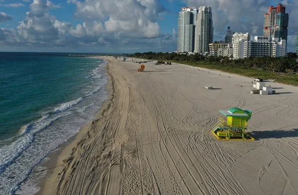 Empty beach with a lifeguard stand, high-rise buildings in the background, and cloudy sky.