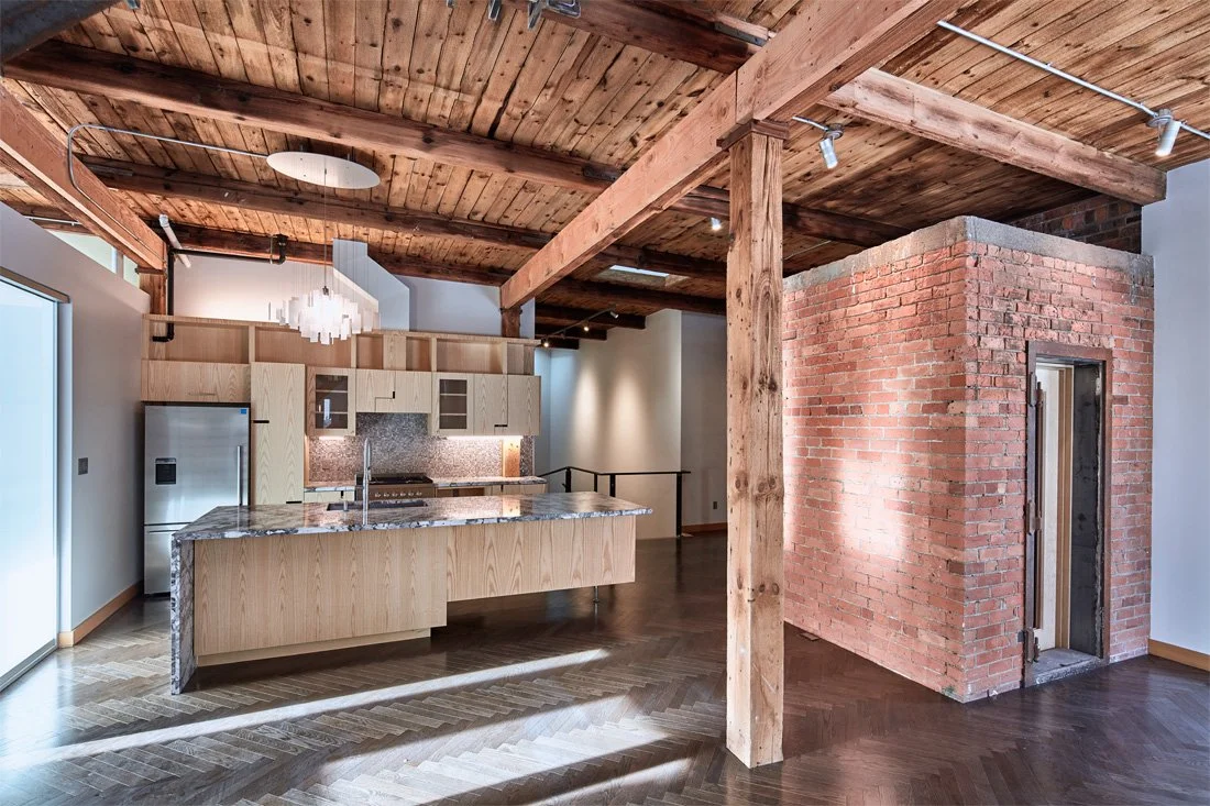 Industrial-style loft interior with exposed timber beams and a freestanding brick structure beside the kitchen area