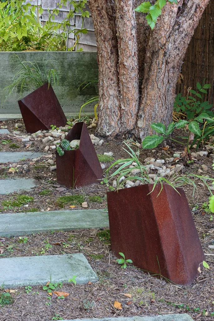 A rustic garden path, lined with angular rusted steel planters