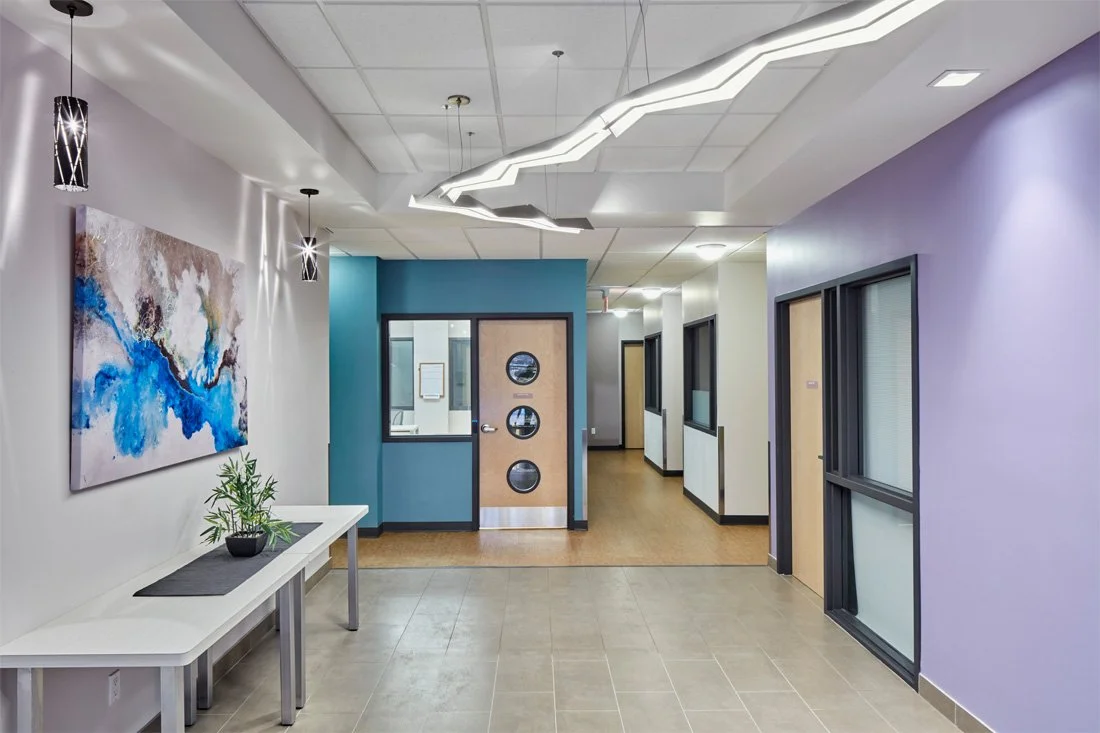 Modern indoor hallway with colorful walls, artwork, decorative lighting, and a potted plant on a bench.