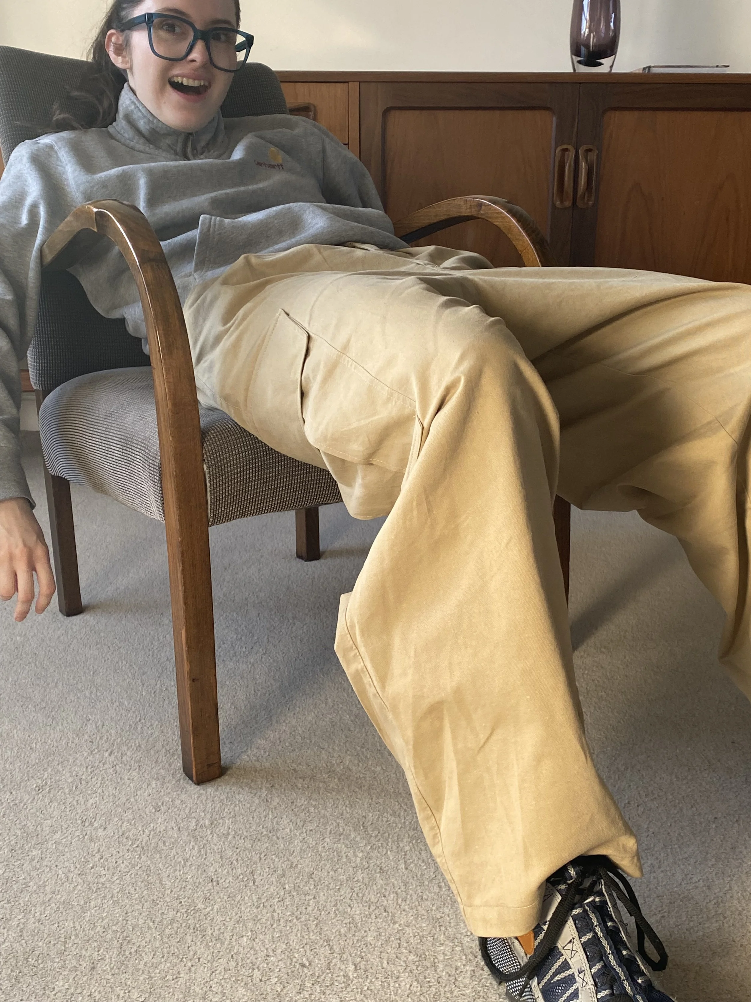 A young woman with glasses sitting in a chair wearing Jericho Pants sewn by SewClothing using Jericho Pants Sewing Pattern.