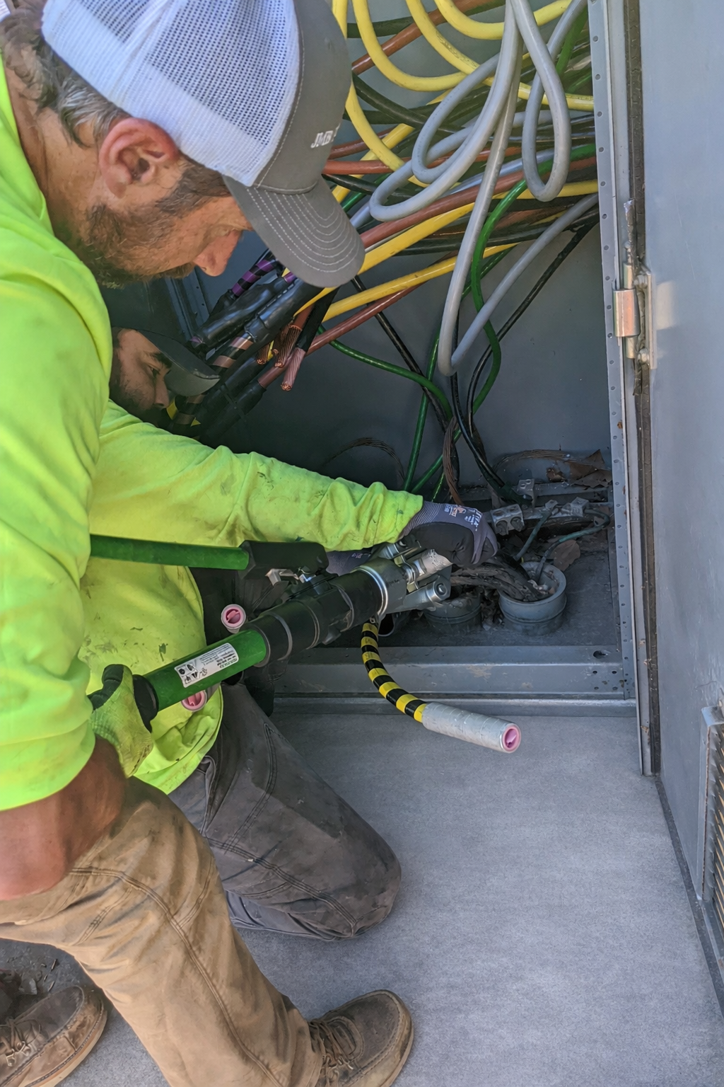 Two technicians working inside an electrical panel with colorful wires and tools.