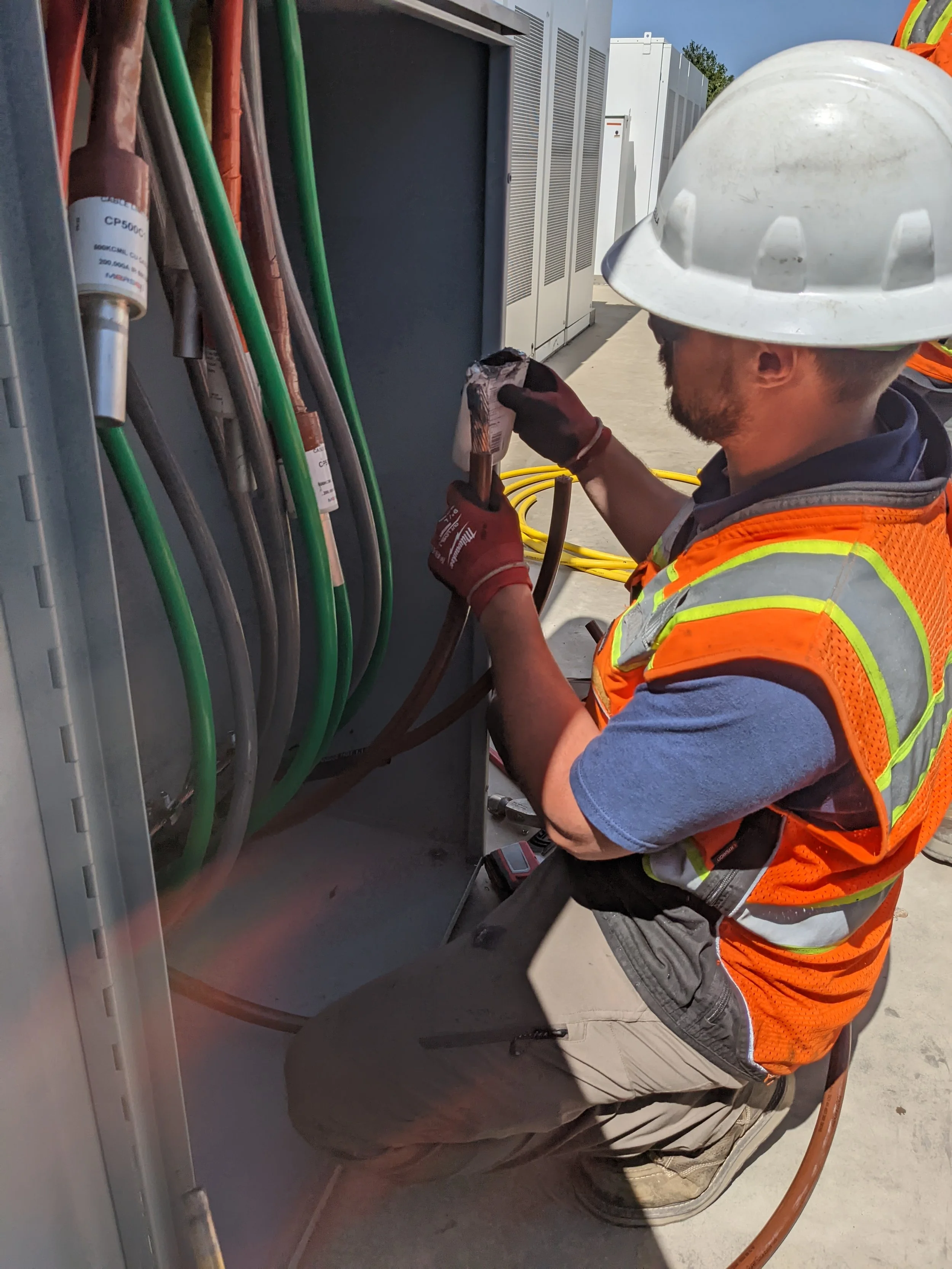 Worker in safety gear repairing electrical wires inside an outdoor electrical panel.