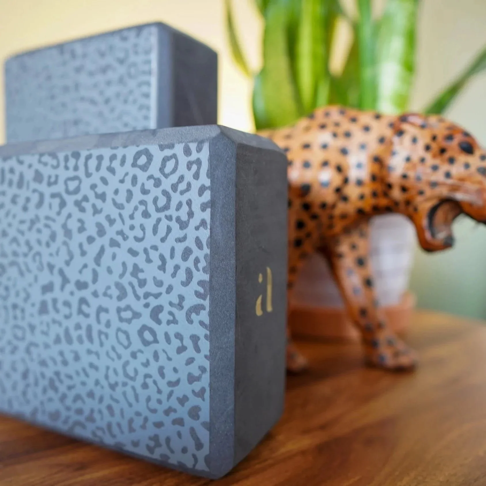 Close-up of a Peterson branded speaker or electronic device with leopard print pattern, with a decorative cheetah figurine in the background on a wooden surface, and a green houseplant nearby.