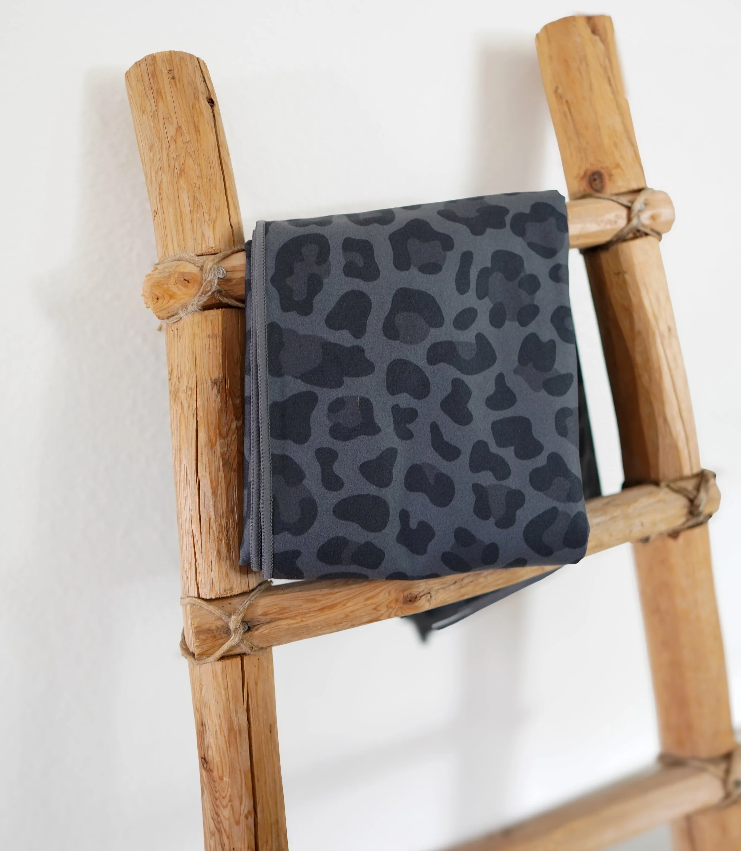 Folded black and gray leopard print clothing item hanging on a rustic wooden ladder against a white wall.