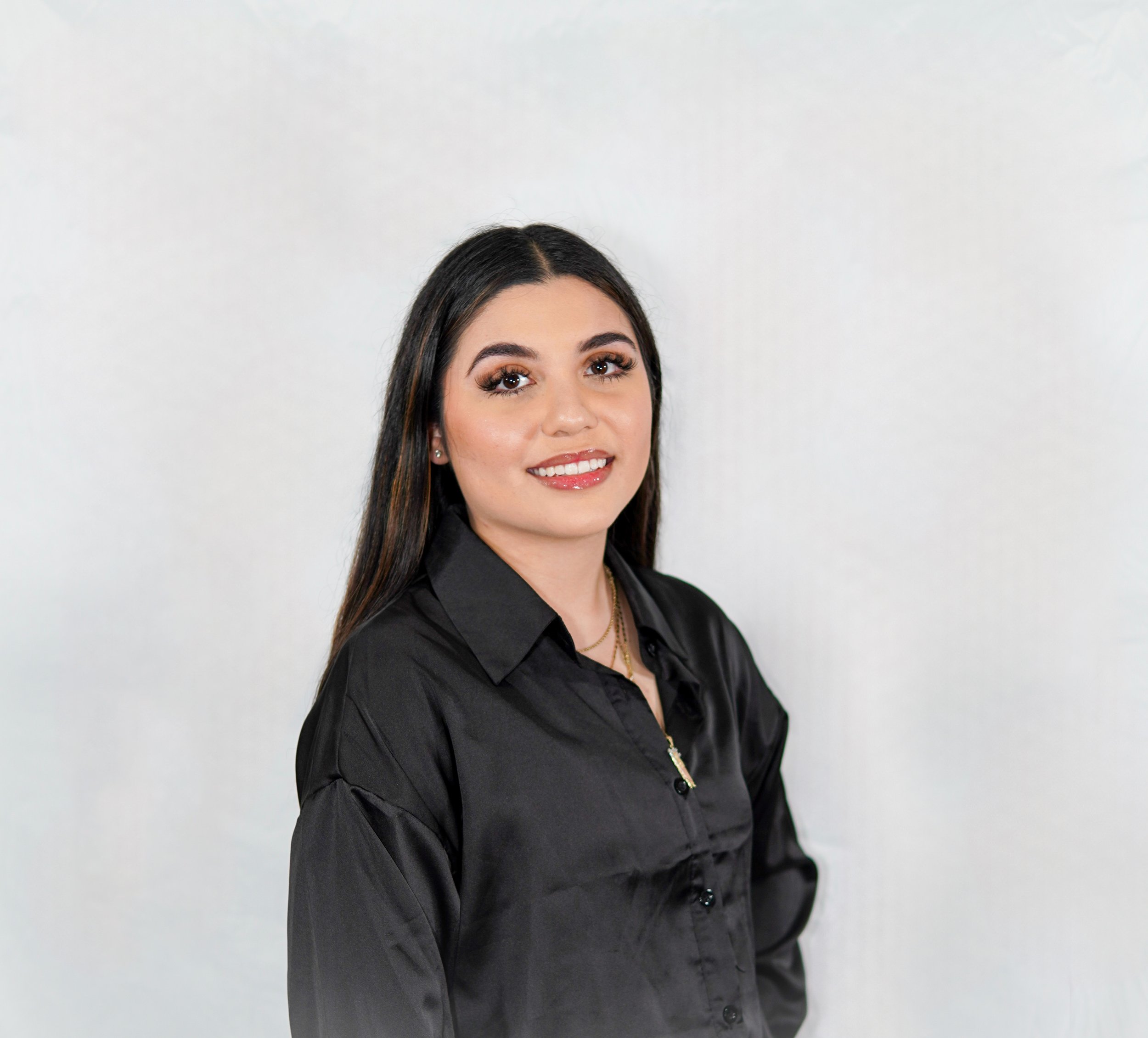 A young woman with long dark hair, wearing a black button-up shirt, smiling at the camera against a plain white background.