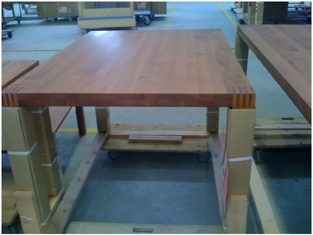 A wooden workbench in a workshop with a wooden table top and metal legs on casters.