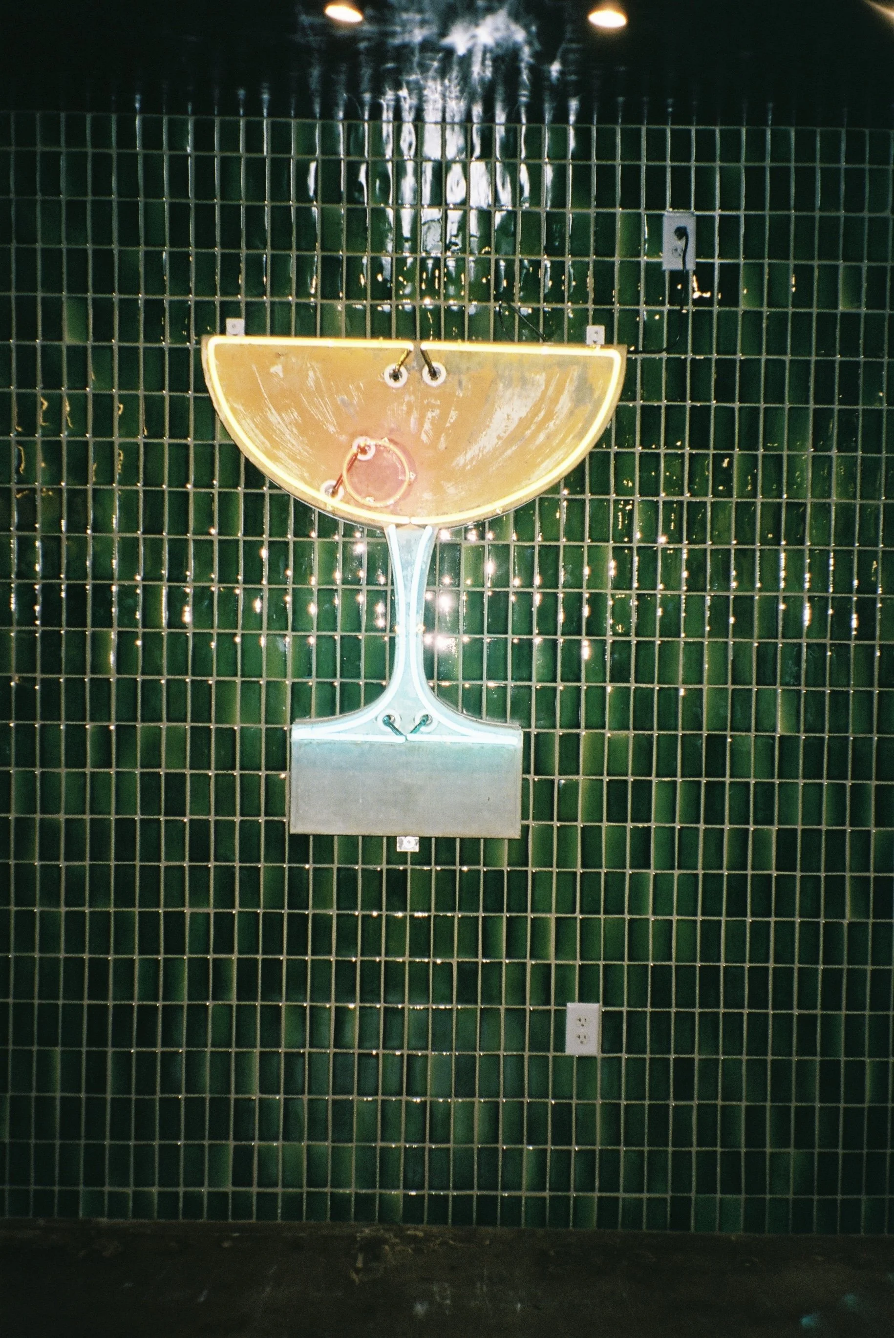 Neon sign shaped like a margarita glass with a slice of lime, mounted on a green tiled wall.