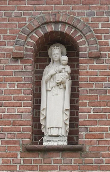 Statue of the Virgin Mary holding baby Jesus, placed in a brick alcove with an arched top.