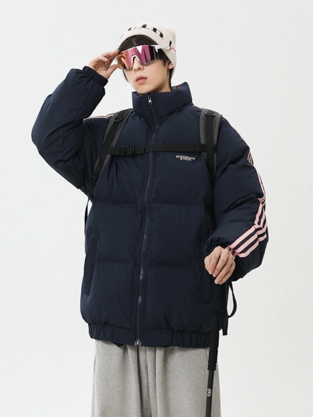 Person wearing a dark jacket, sunglasses, and a beige hat, holding a walking stick.